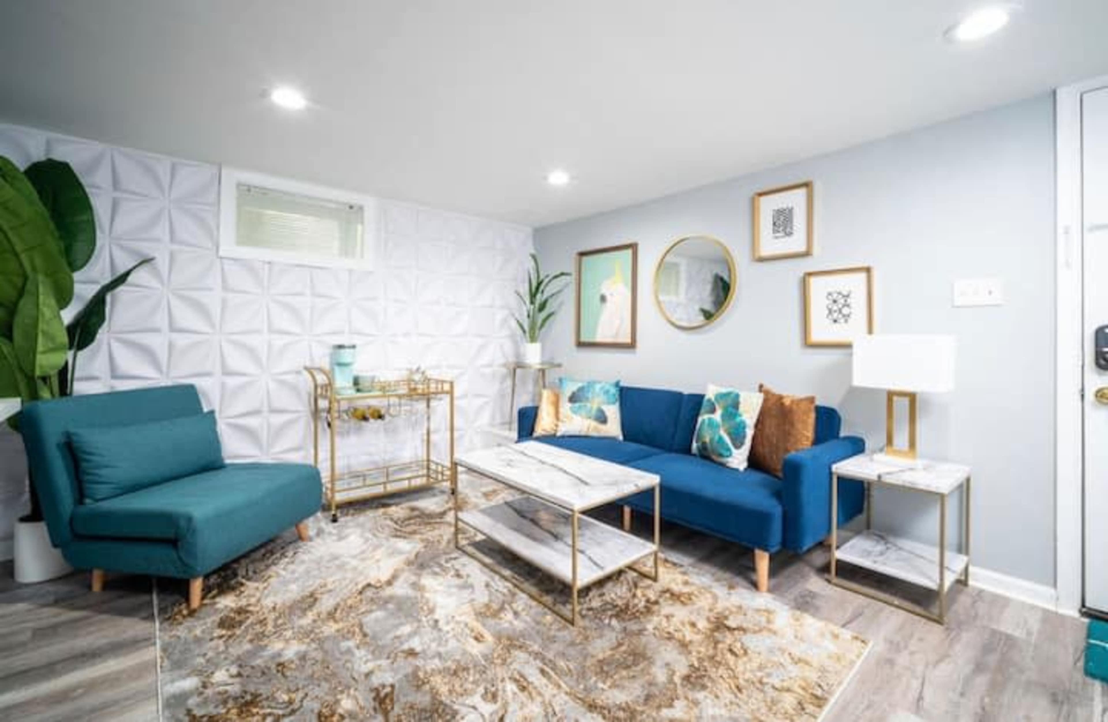 A modern living room with a blue couch, a green accent chair, a marble coffee table, and decorative wall art.