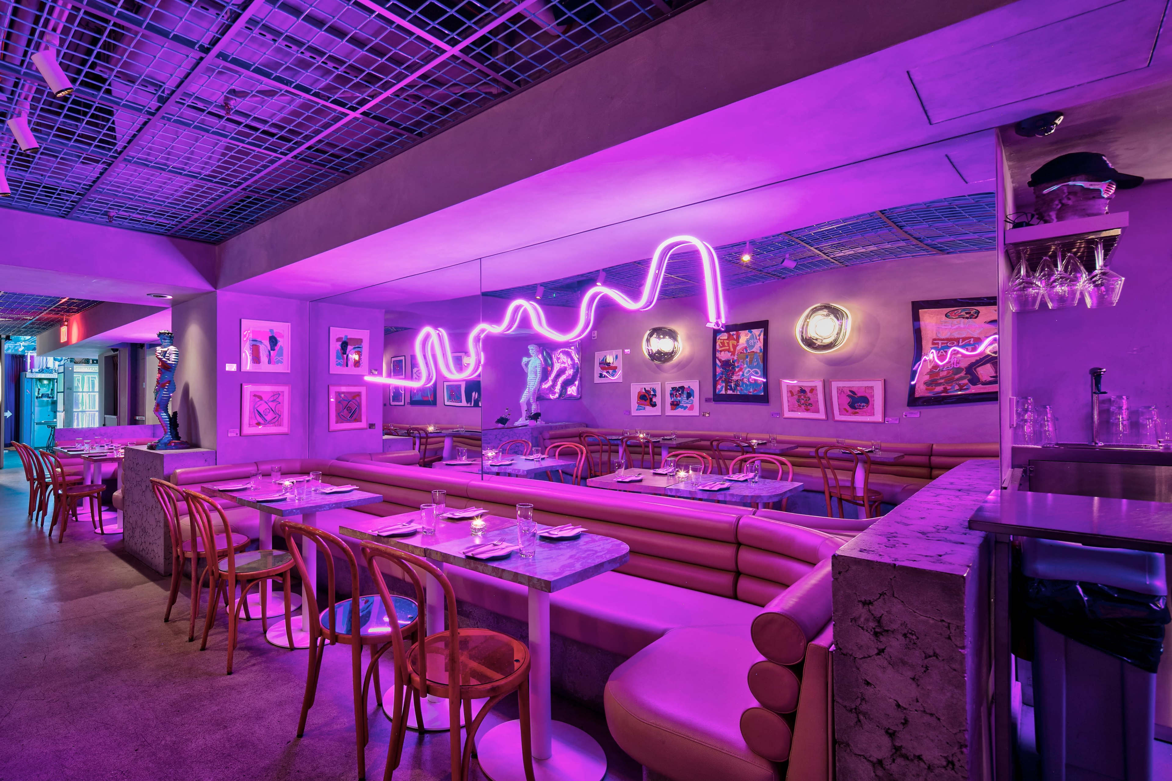 The image shows a modern restaurant interior with pink neon lighting, featuring curved seating and colorful artwork on the walls.