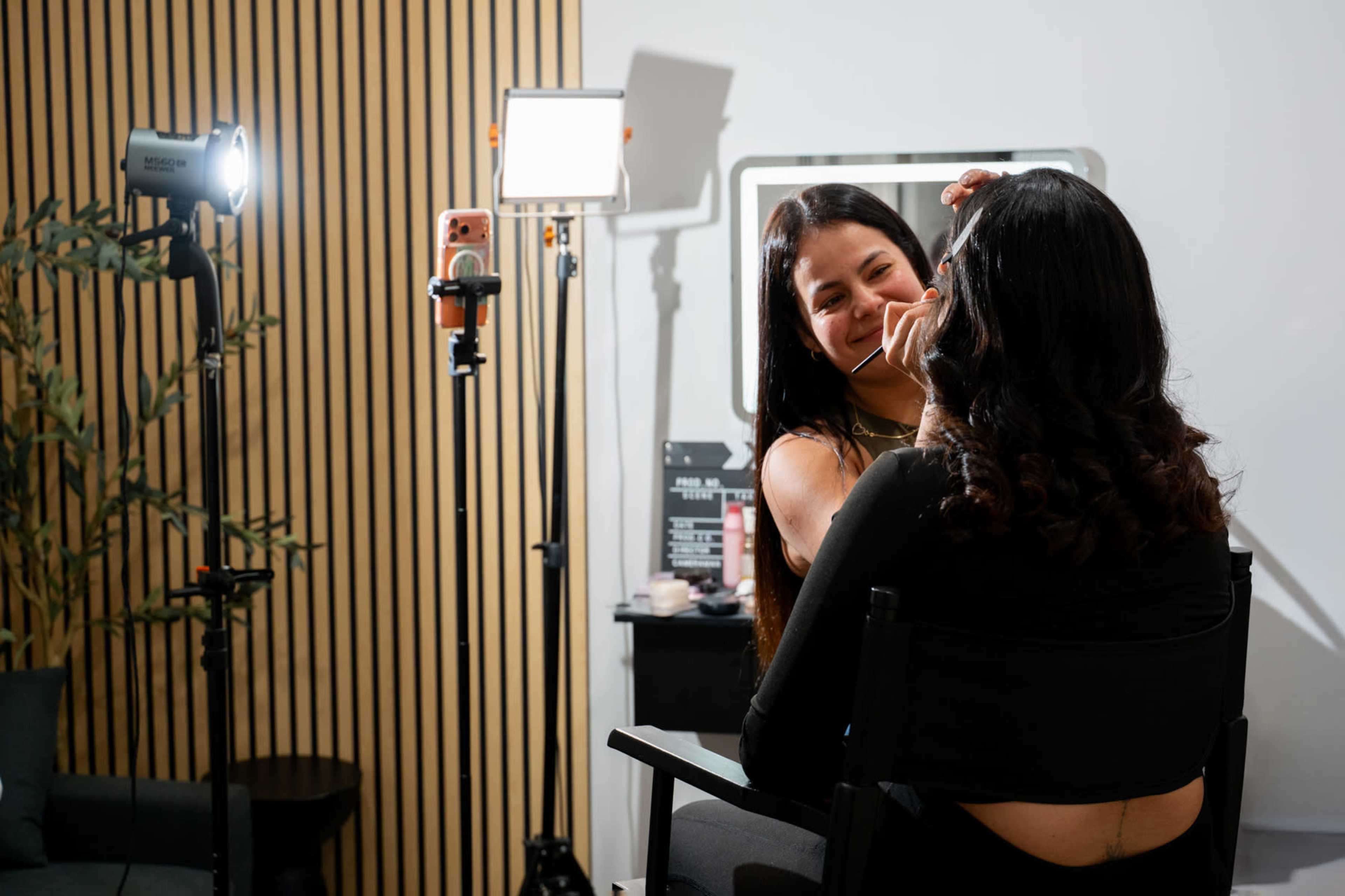A makeup artist applies makeup to a client in a well-lit salon setting.