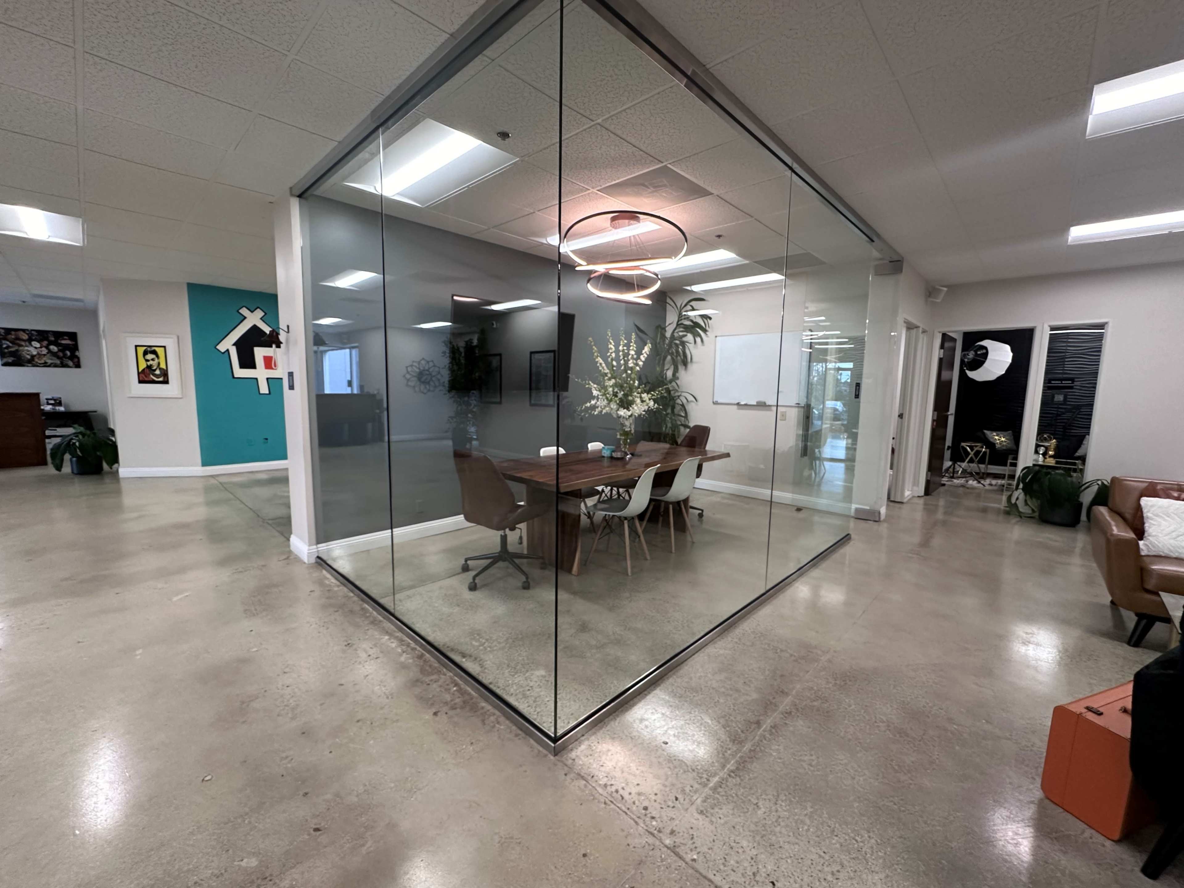 A modern office space featuring a glass-walled meeting room with a wooden table and chairs, surrounded by a minimalist decor.