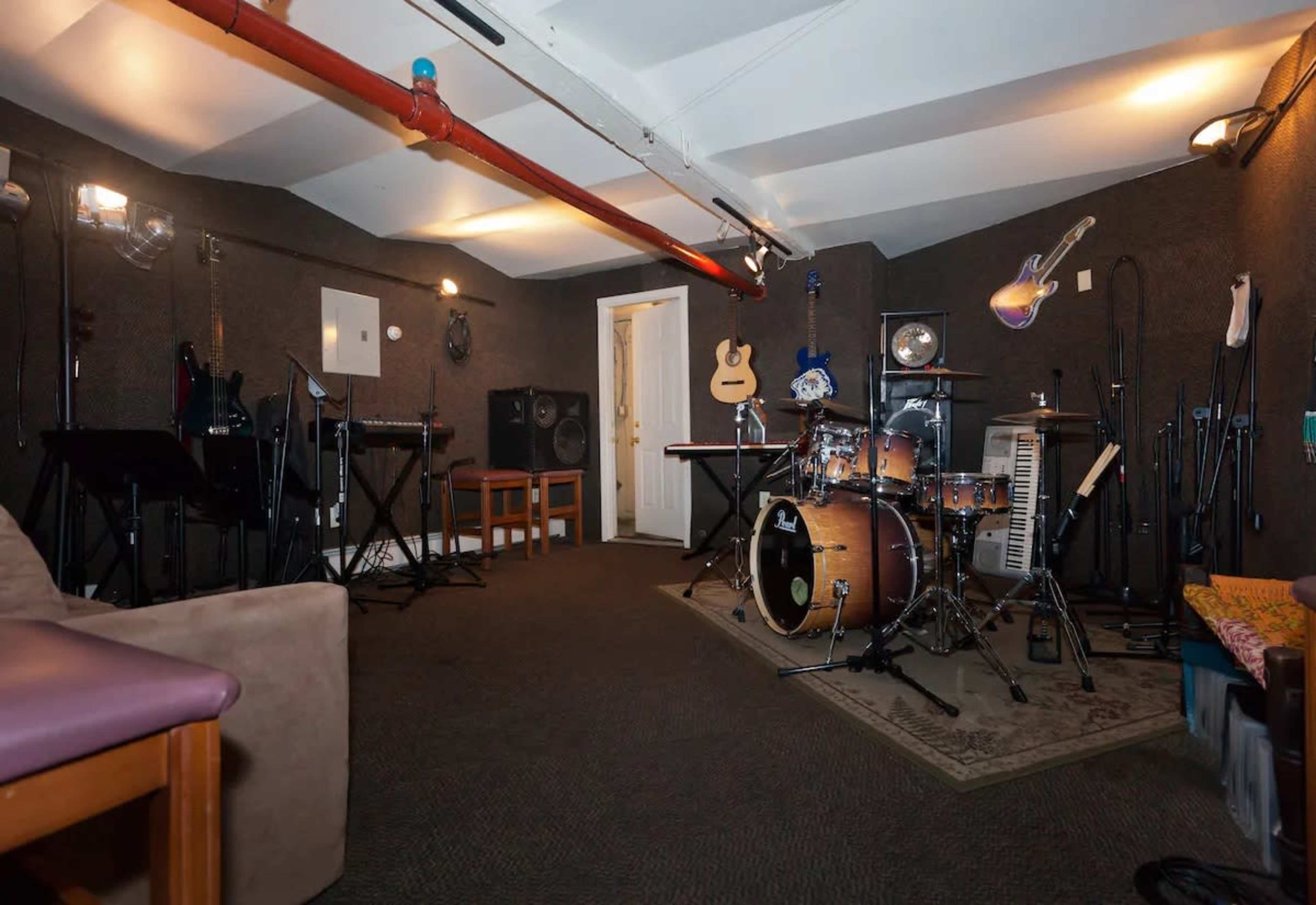 A soundproof music studio featuring a drum set, several guitars, keyboards, microphones, and audio equipment arranged around the room.