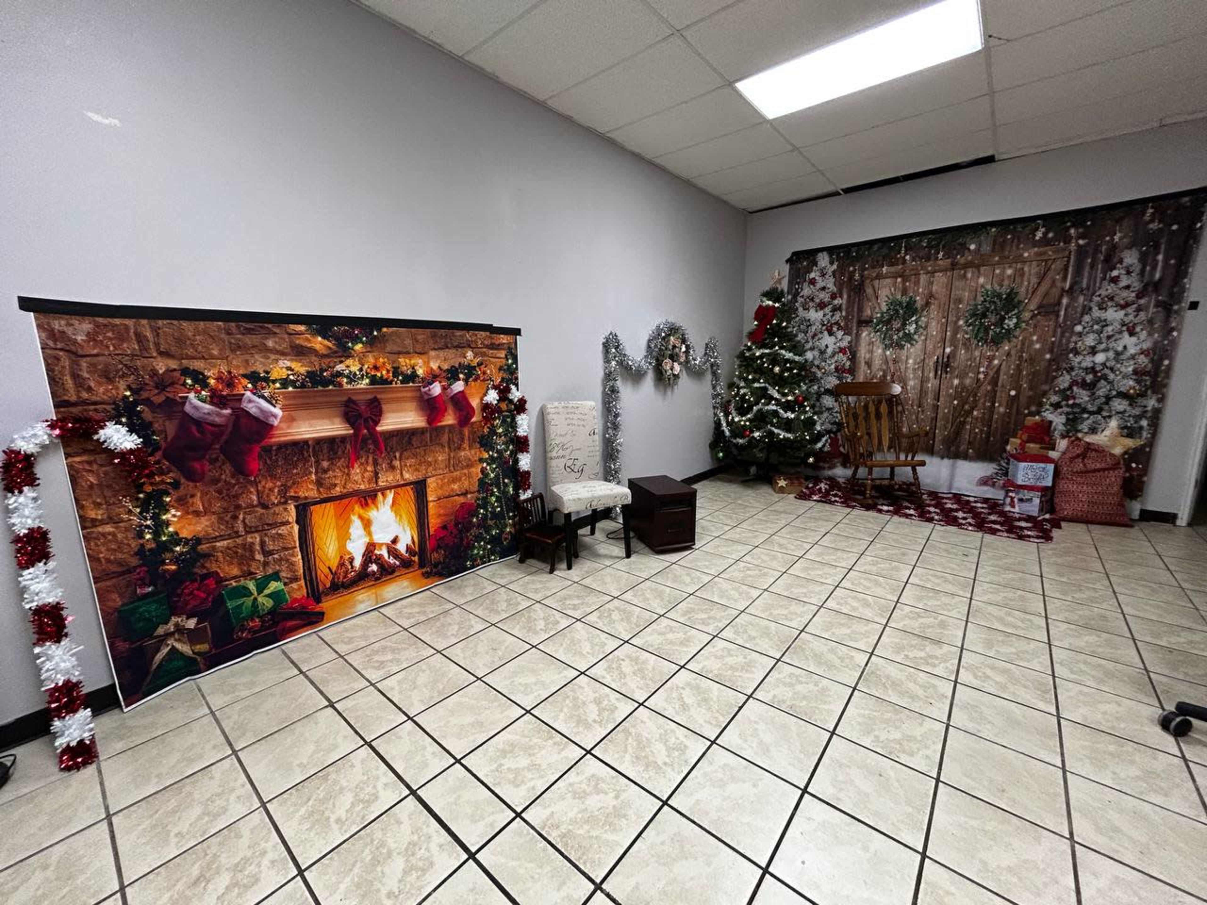 A decorated room featuring a faux fireplace with stockings, a Christmas tree, and festive props arranged along the walls.