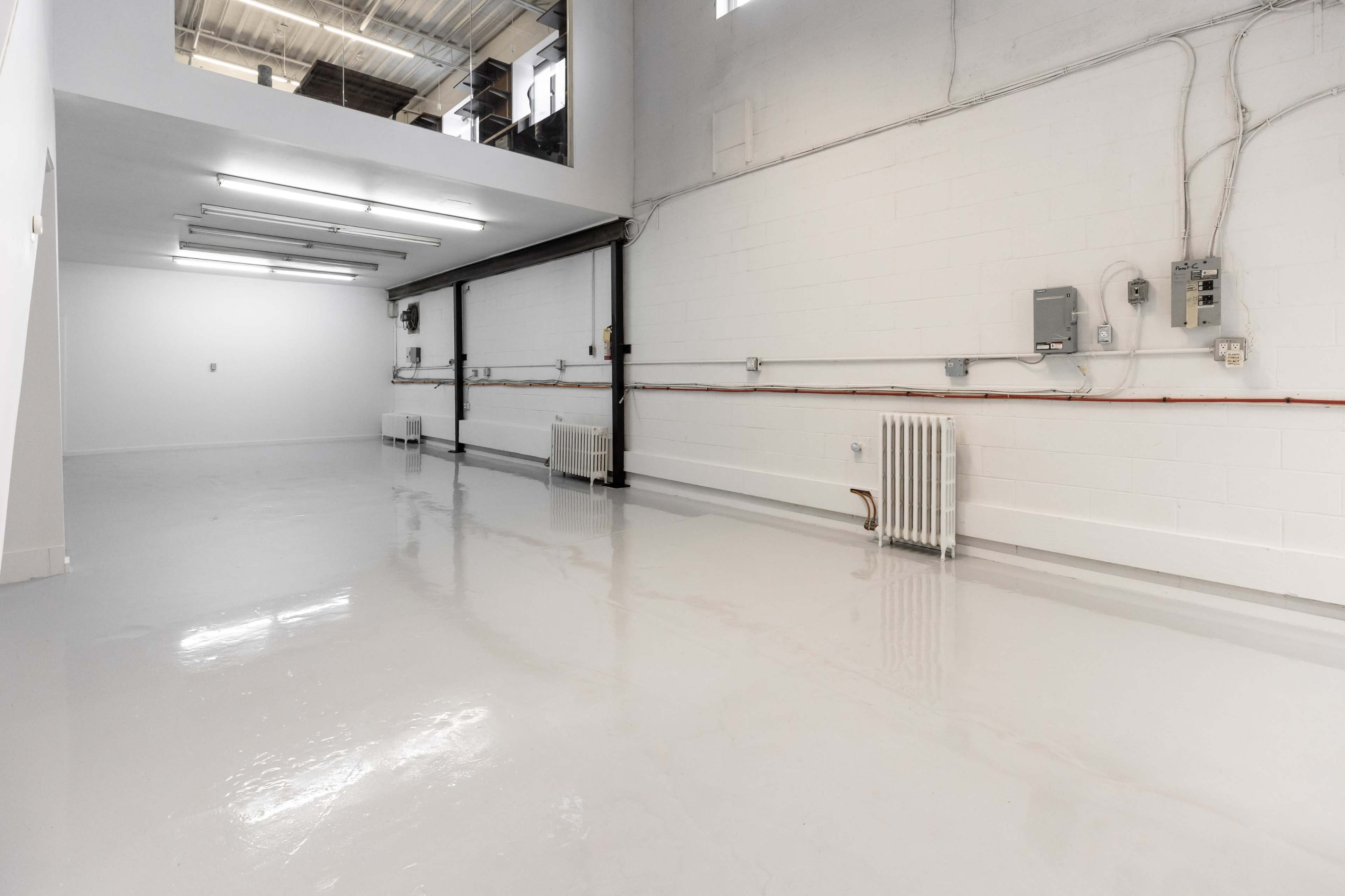 The image shows a spacious, empty room with a glossy white floor, white walls, and exposed electrical wiring along the walls.