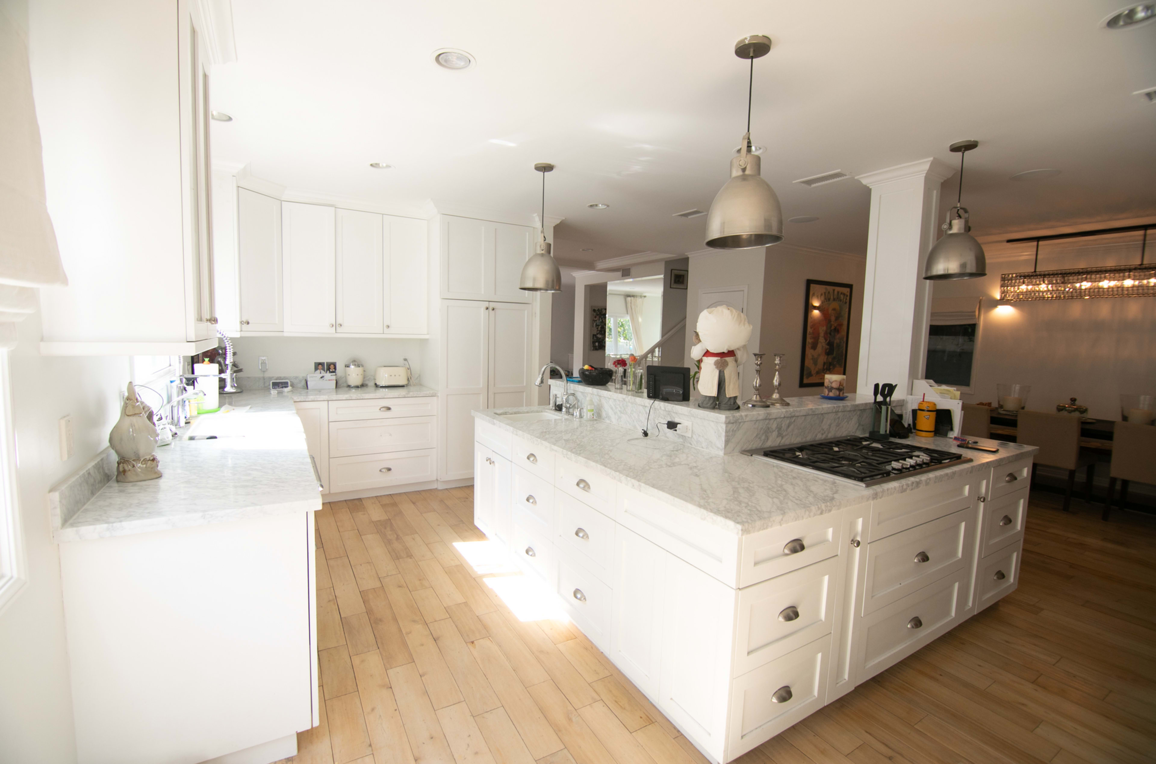 A spacious kitchen features white cabinetry, a large marble island with a gas stove, and pendant lighting.