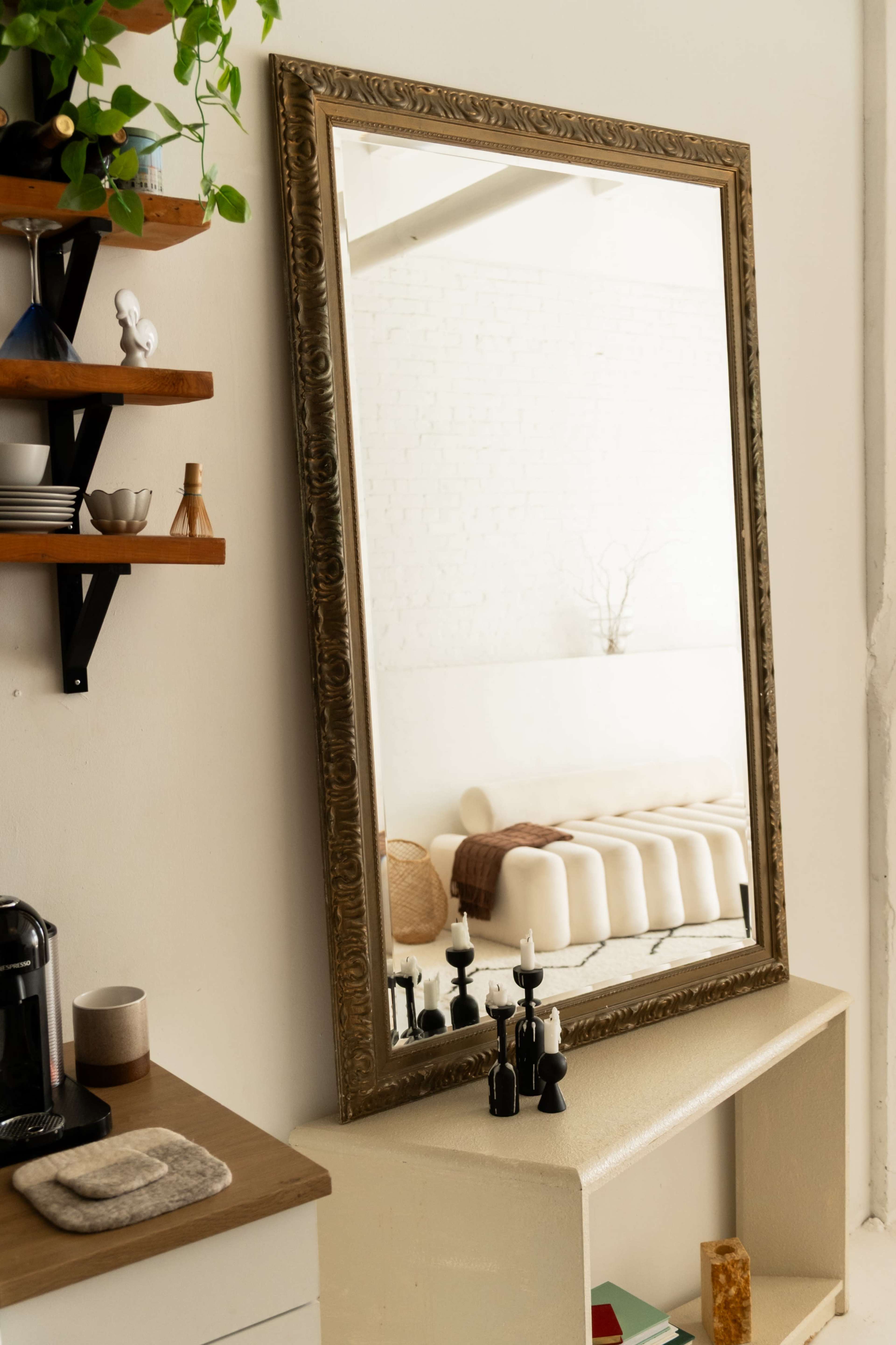 A large ornate mirror is leaning against a wall near a small kitchen area with a coffee maker and a shelf displaying various items.