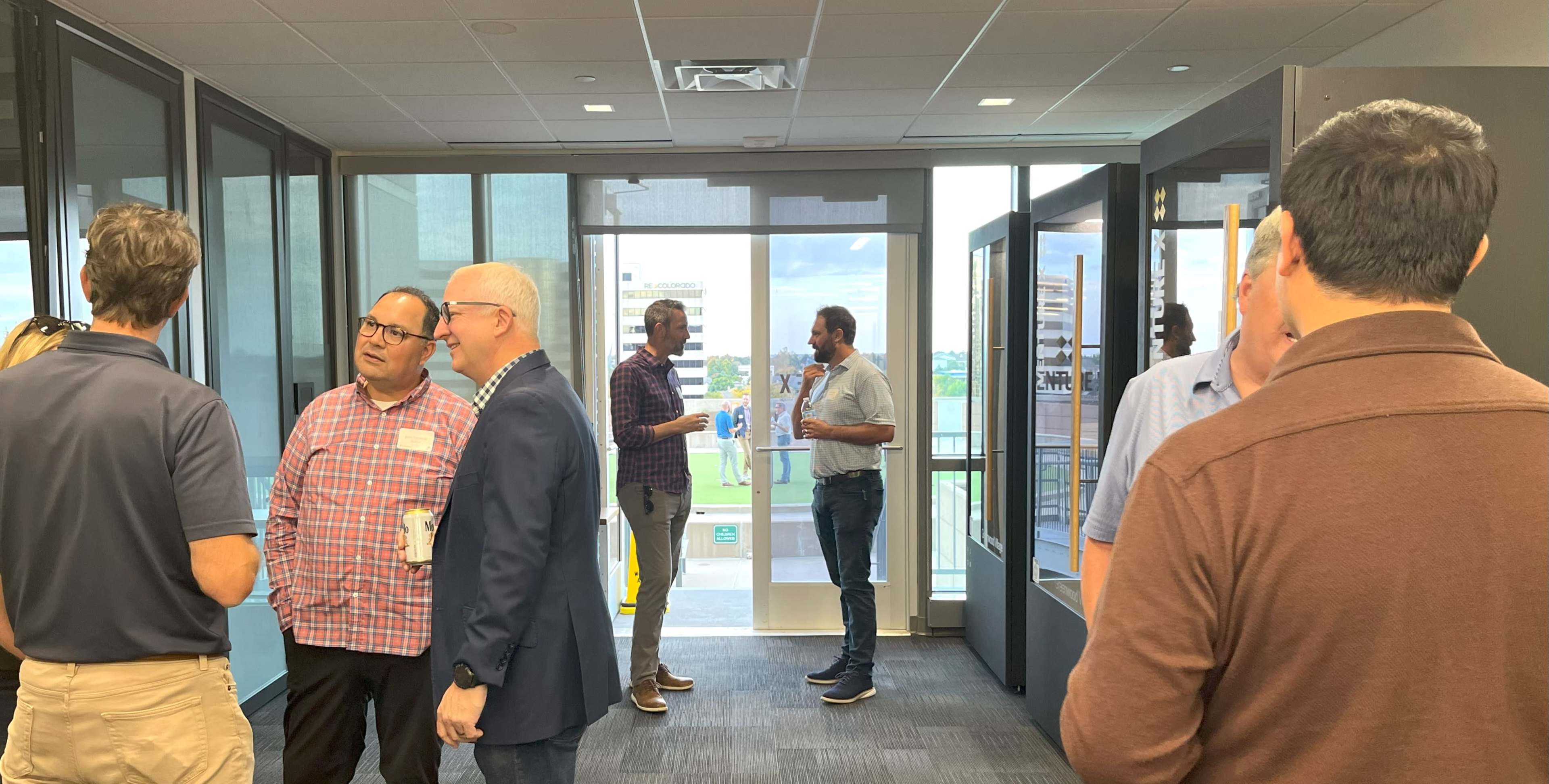 A group of people is conversing in a modern office space, with large windows showing an outdoor view.