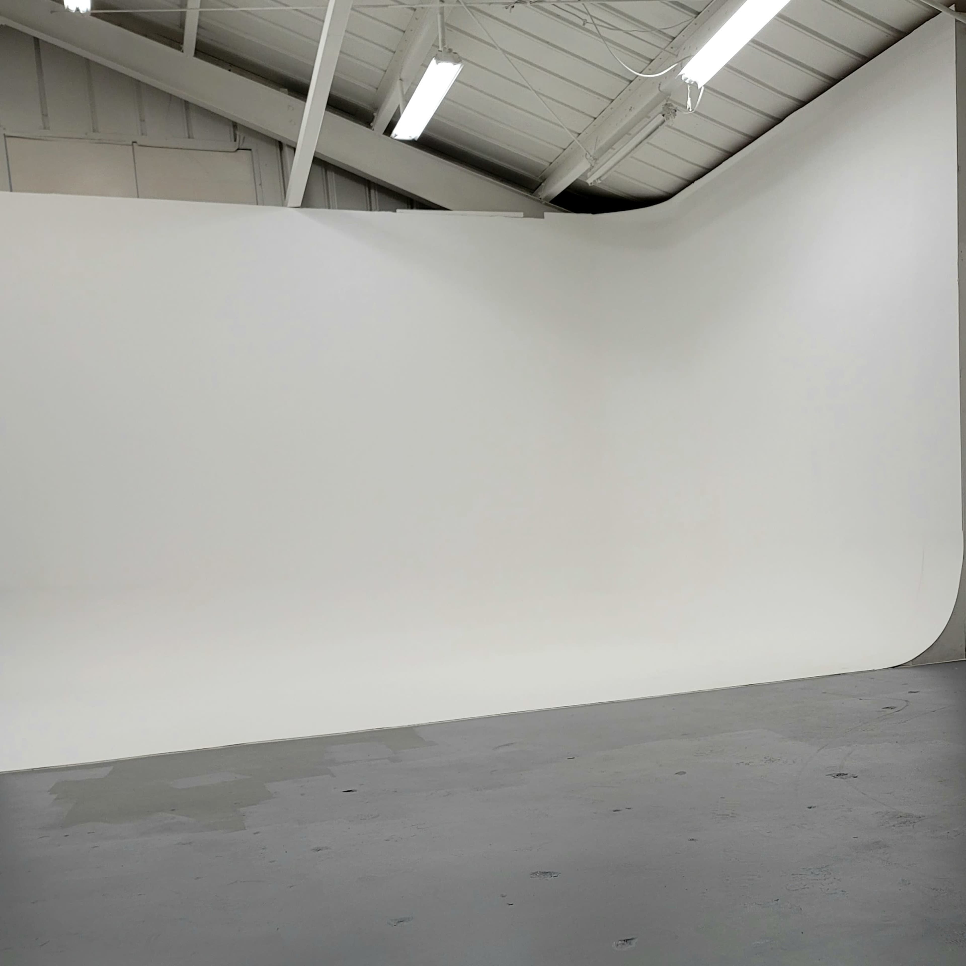 A spacious photography studio with a seamless white backdrop and gray flooring.
