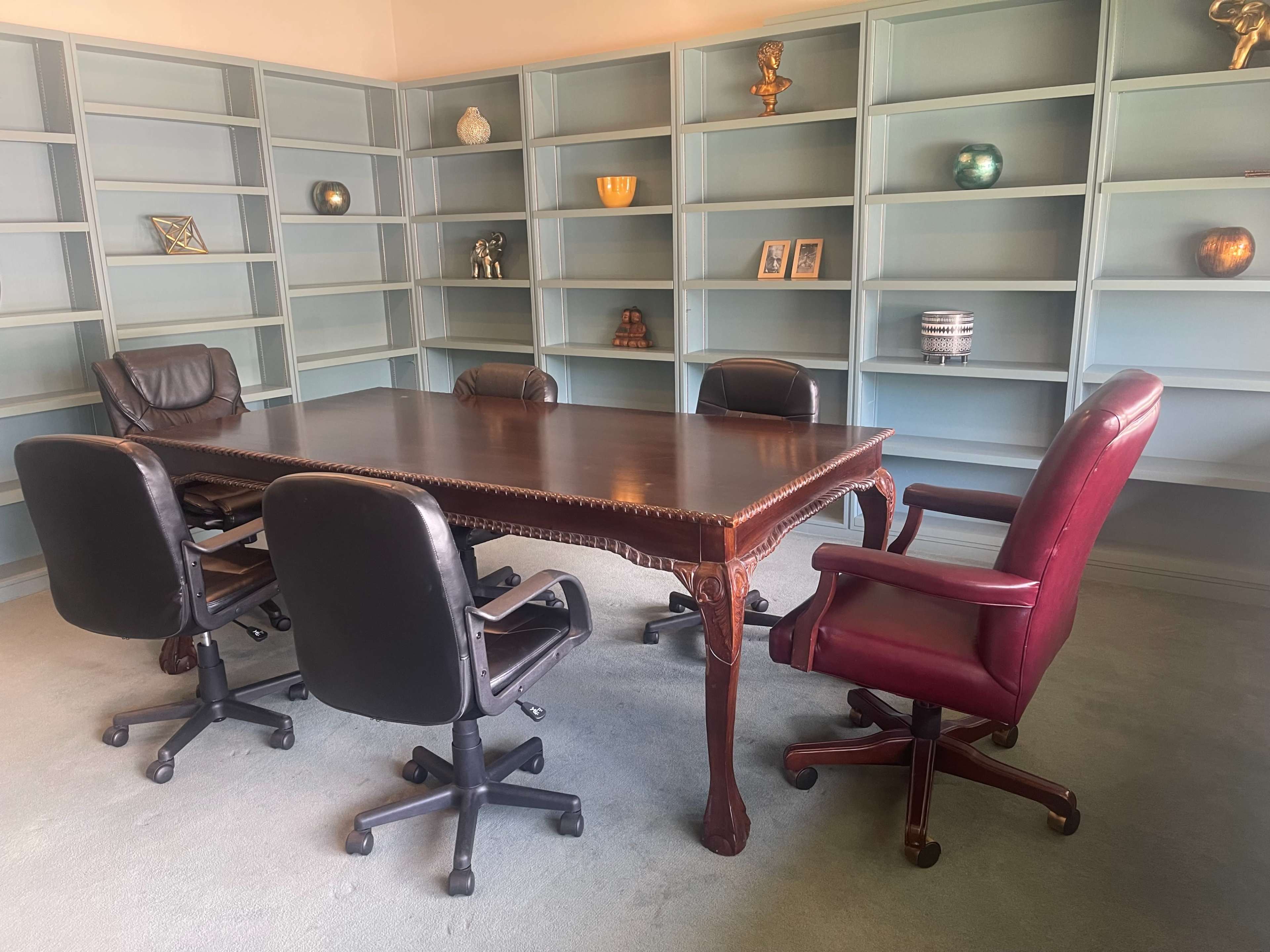 A large wooden conference table is surrounded by six office chairs in a room with light blue shelves displaying decorative items.