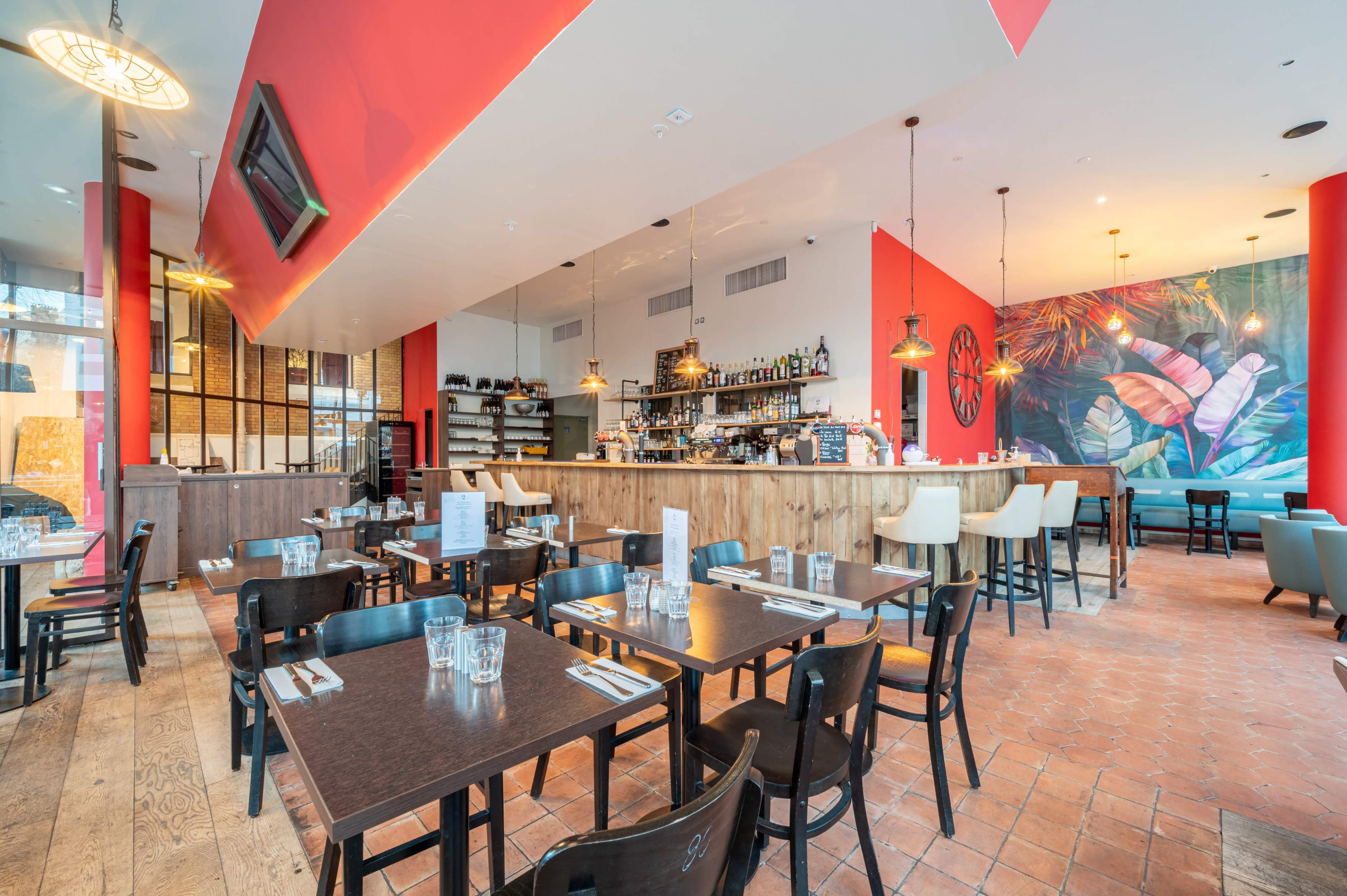 A modern restaurant interior with wooden tables, black chairs, a bar area, and a colorful mural on one wall.