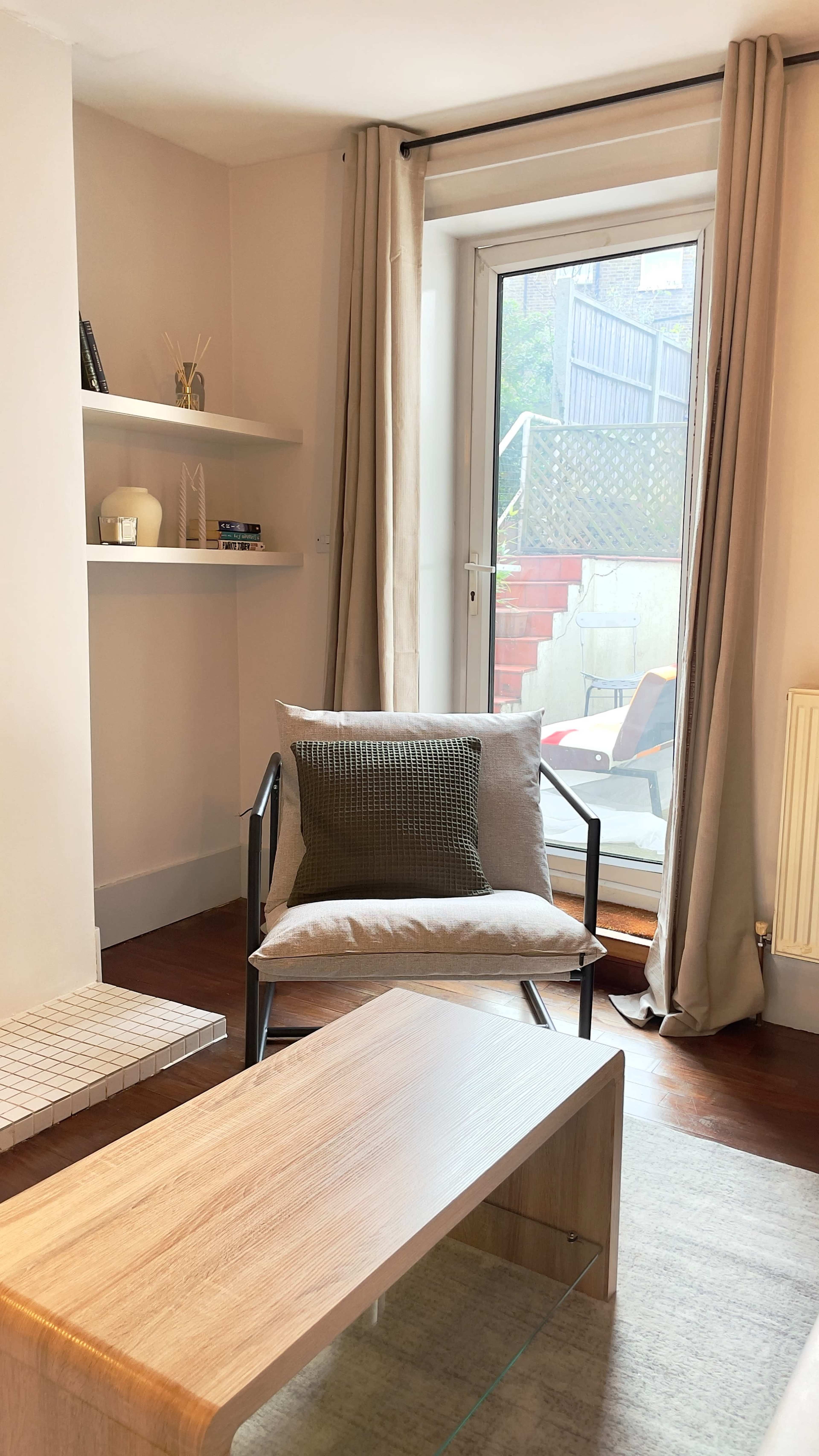 A chair and a wooden coffee table are positioned in a bright room with a sliding glass door leading to an outdoor area.