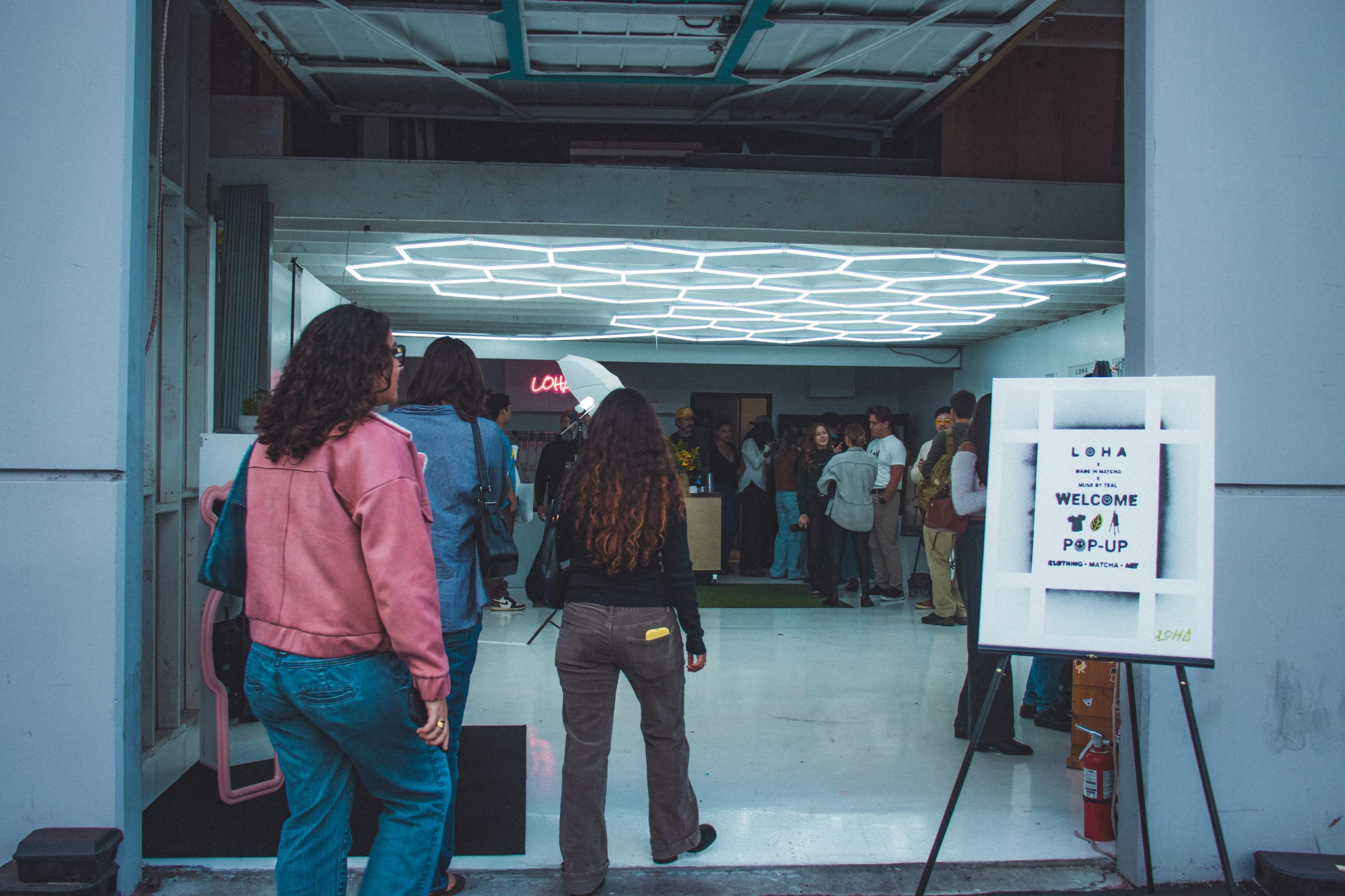 A group of people enters a brightly lit pop-up event space, with a sign welcoming attendees.