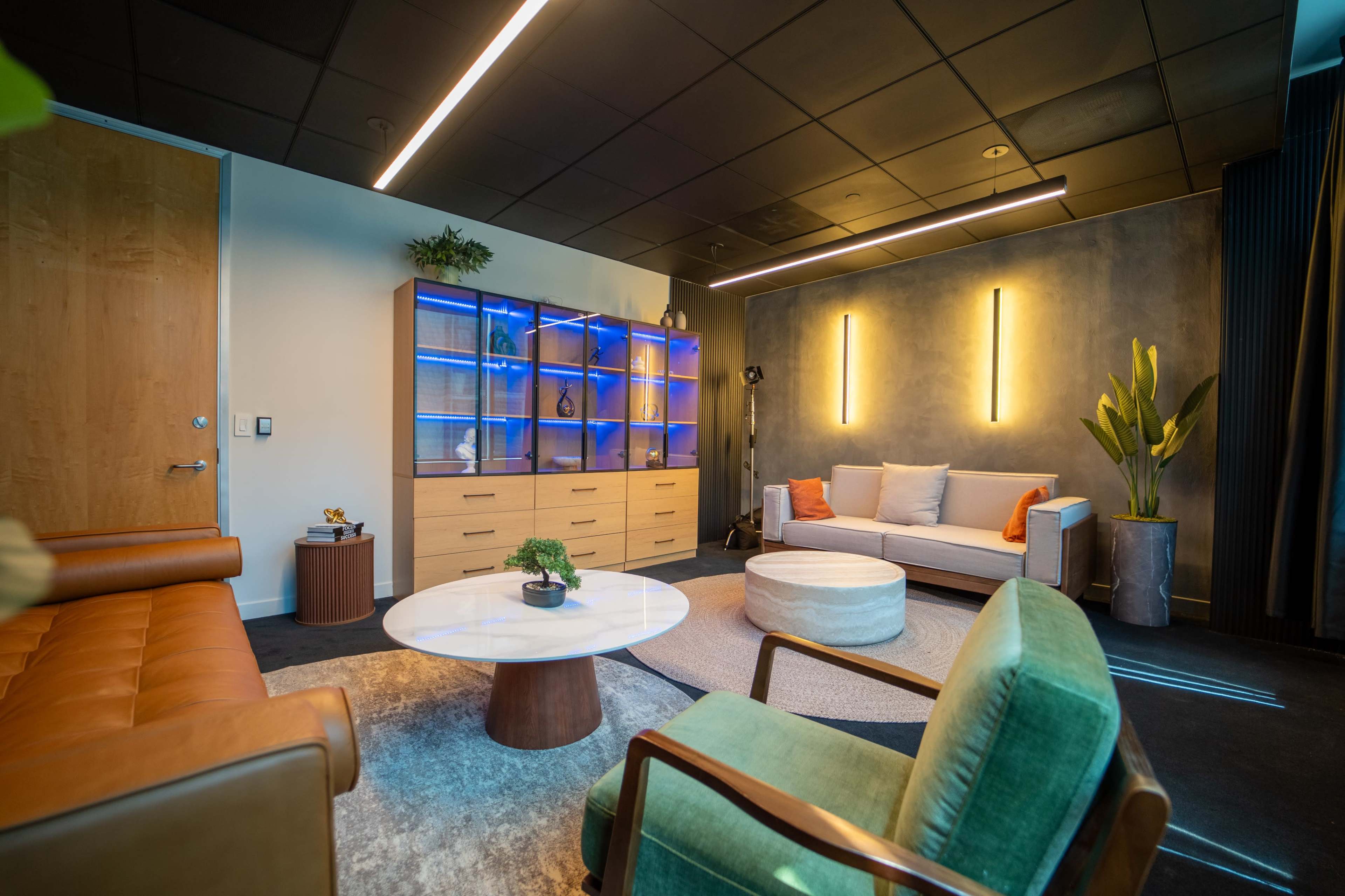 The image shows a modern lounge area featuring a combination of seating options, a coffee table, and a display cabinet with blue lighting.