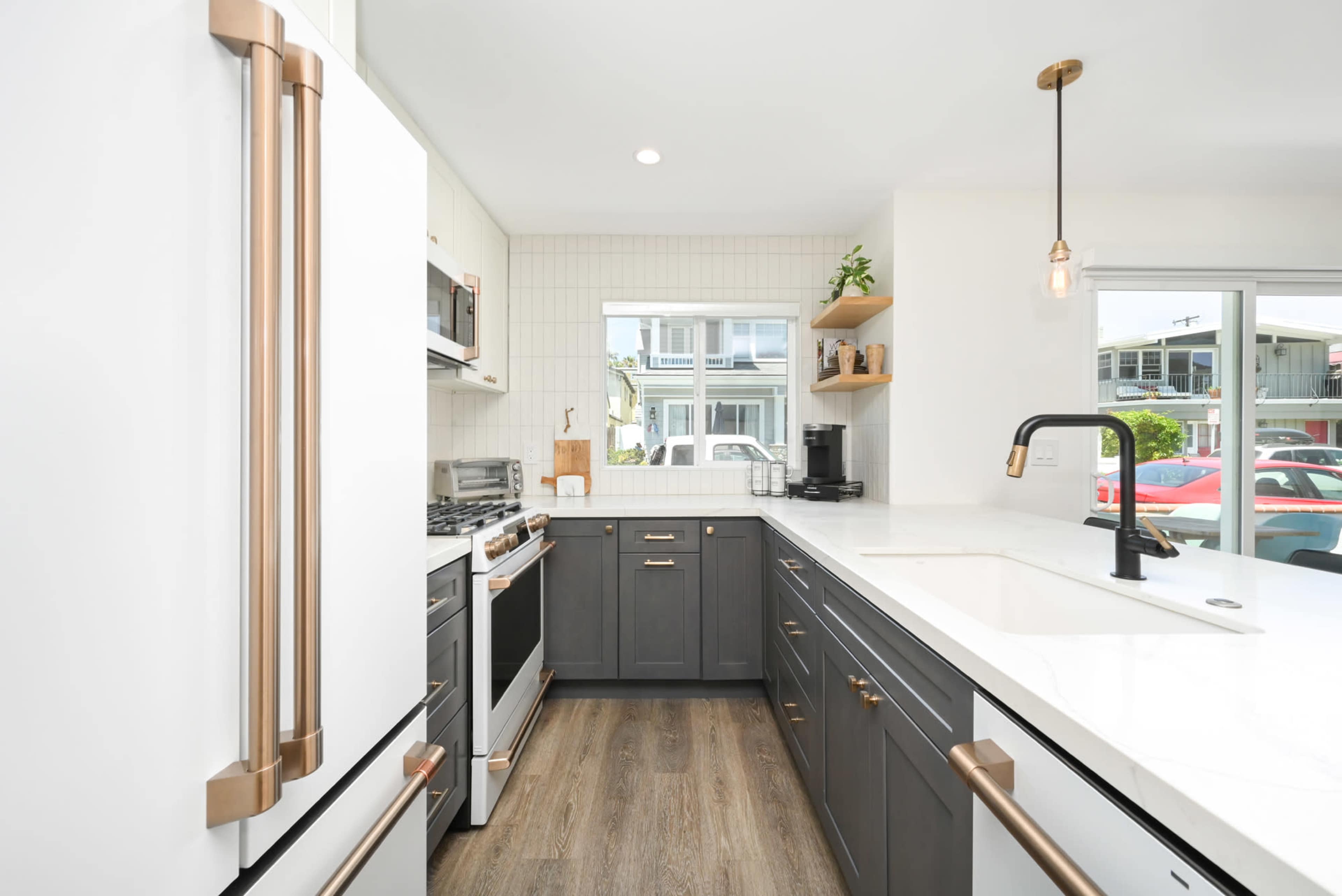 A modern kitchen features stainless steel appliances, dark cabinetry, and a white countertop with a sink near a window.