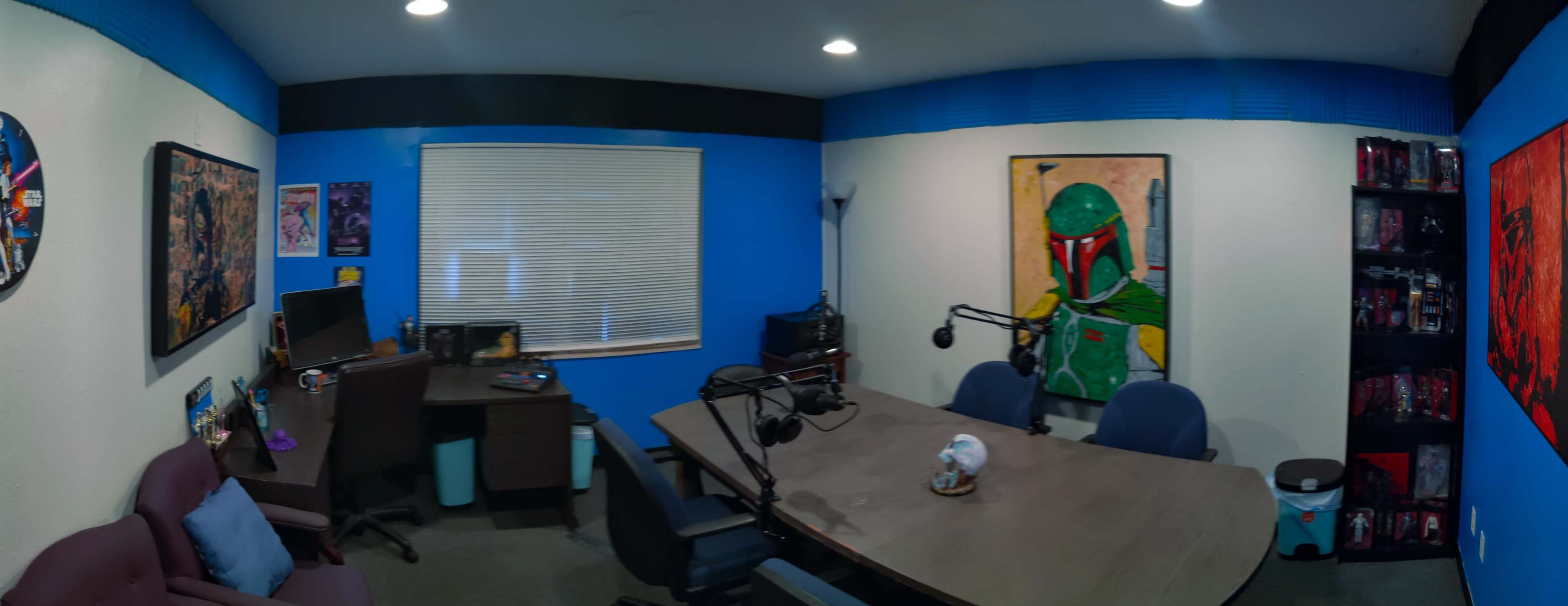 A brightly colored room set up as an office or podcast studio, featuring a large table, chairs, and decorations including artwork on the walls.
