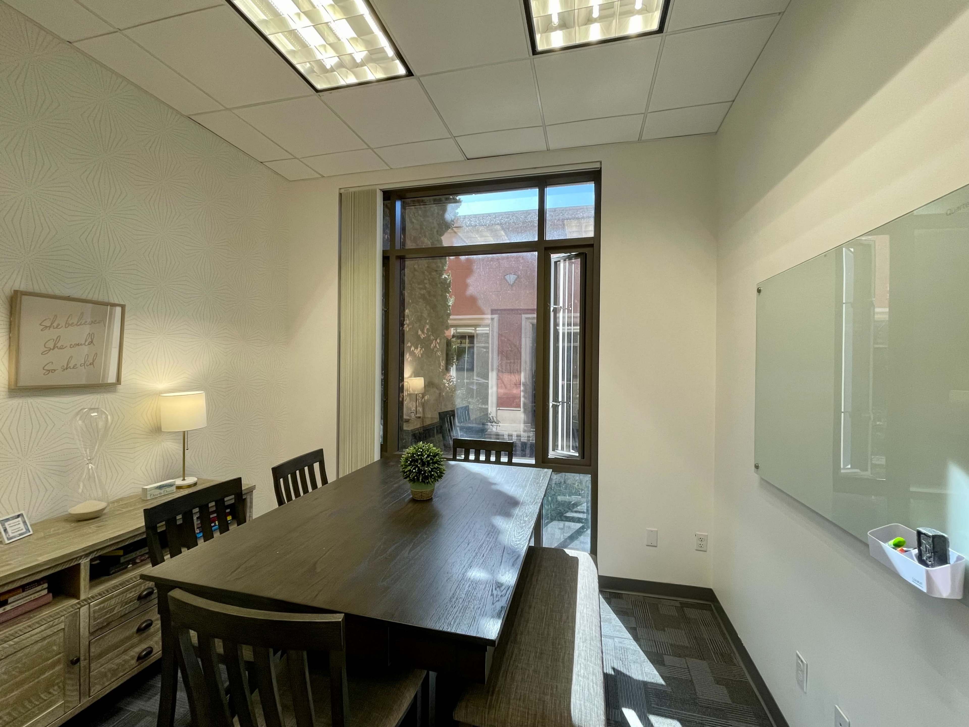 A meeting room features a large wooden table, a window overlooking a courtyard, and a whiteboard on the wall.