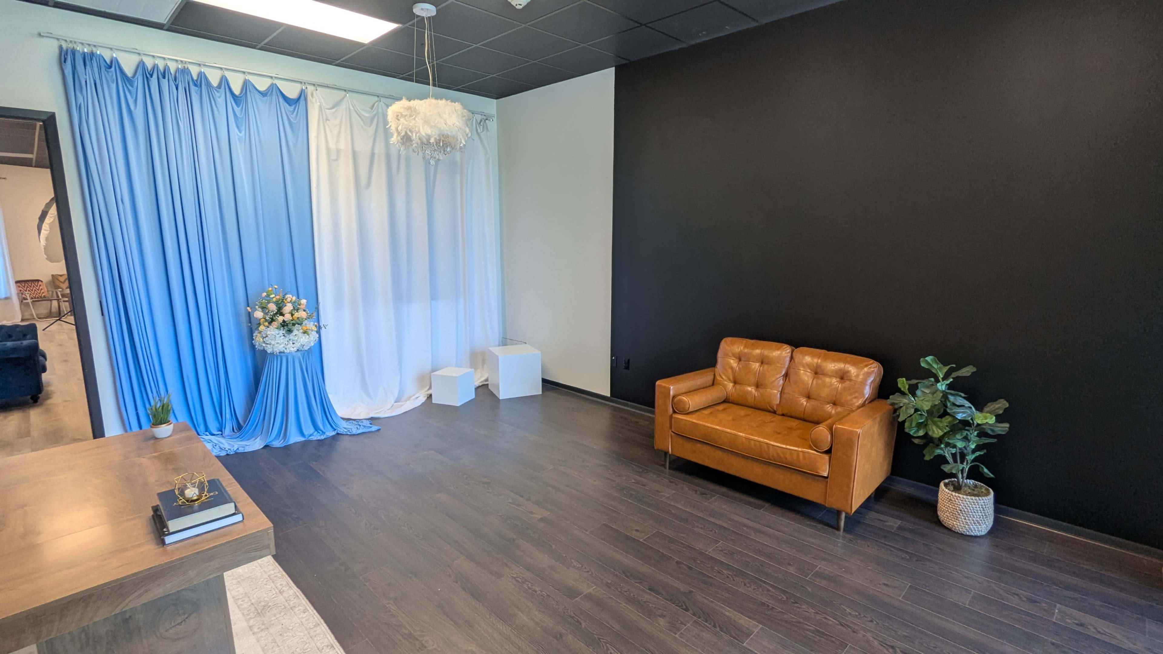 The image shows a small, modern interior space featuring a brown leather sofa, a decorative flower arrangement, and a blue and white backdrop, set against a black wall.