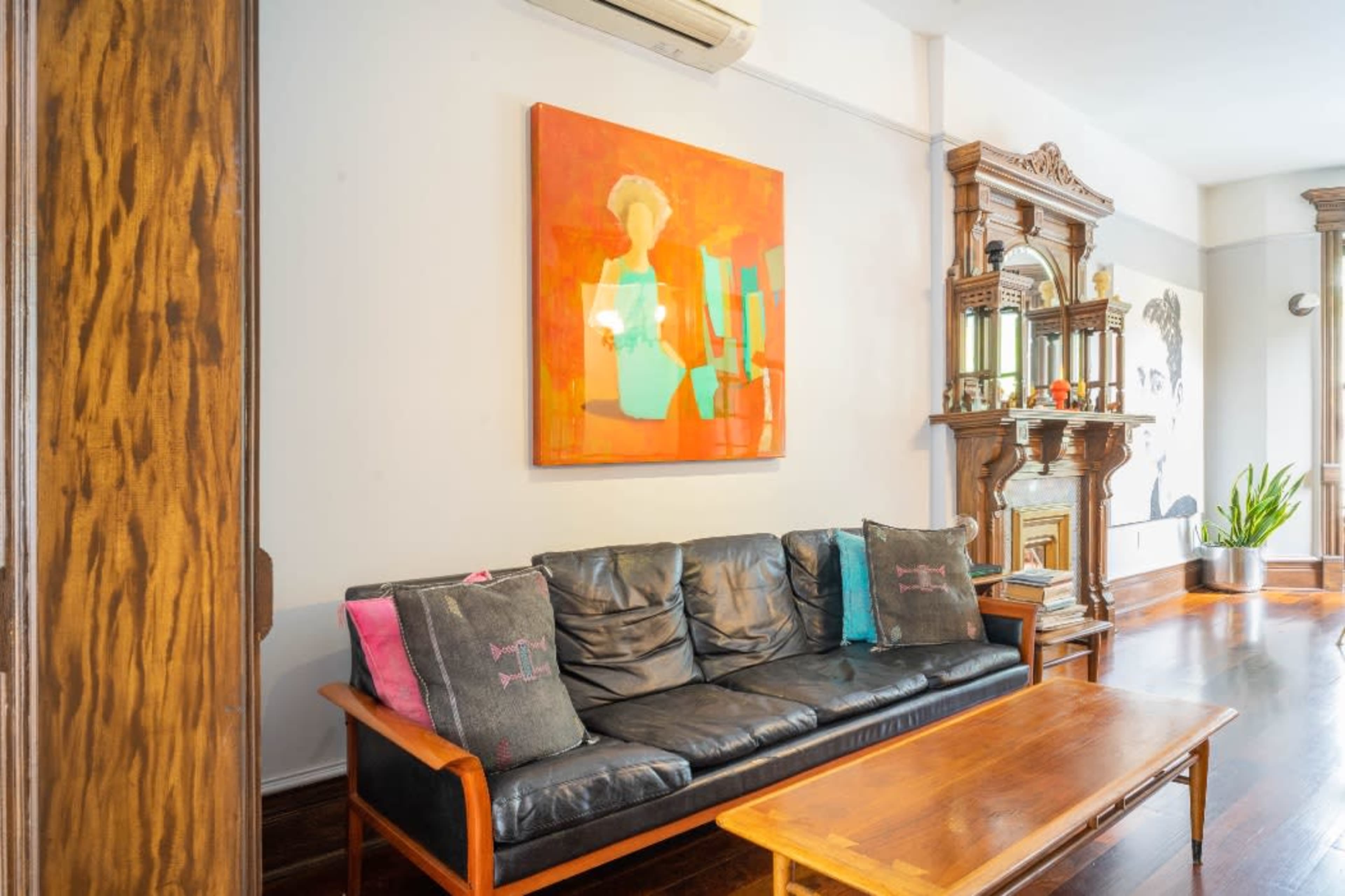 The image features a living room with a black leather couch, a wooden coffee table, a large colorful painting on the wall, and an ornate wooden furniture piece in the background.