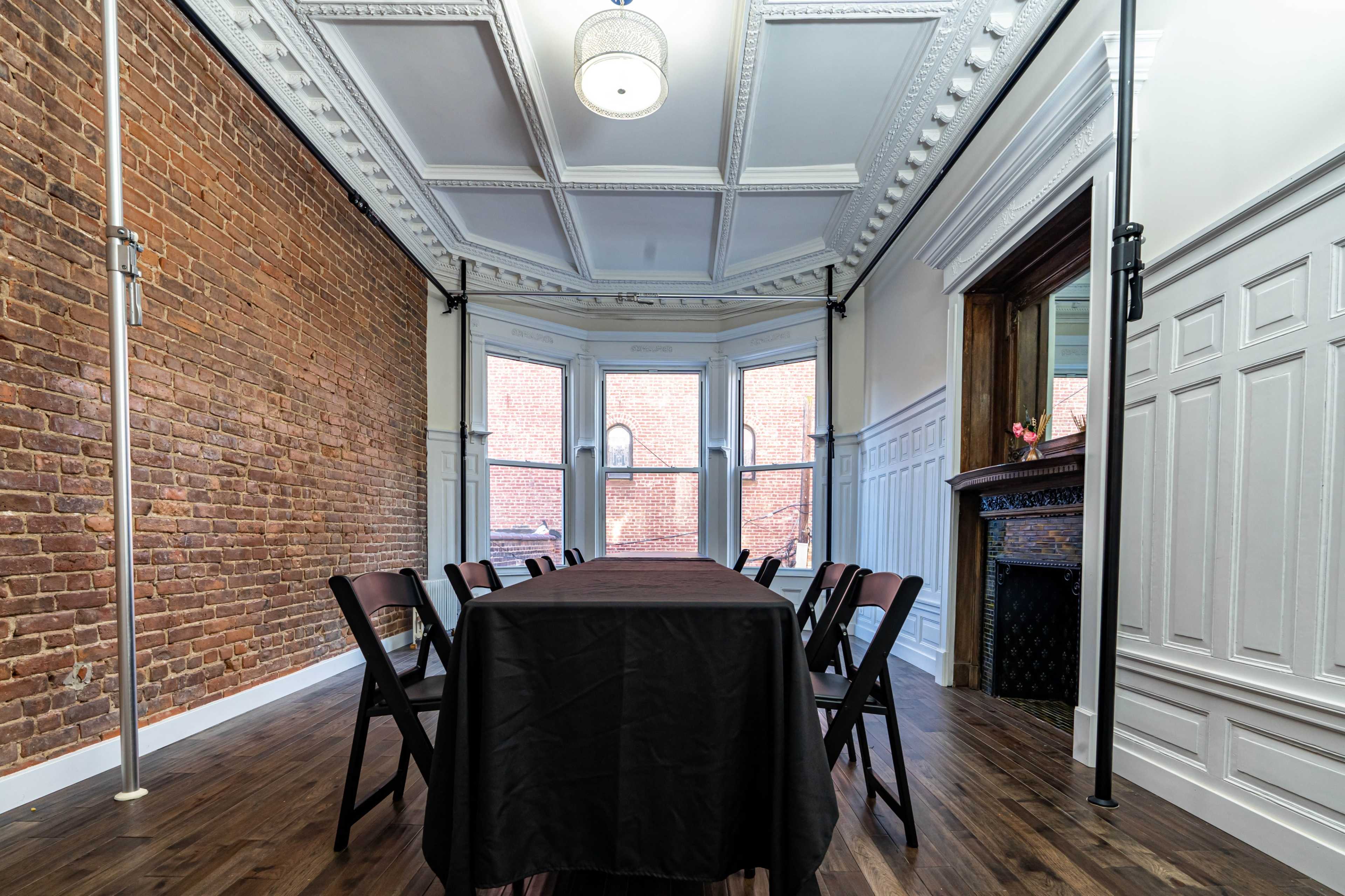 A conference room features a long table with chairs, brick and white-paneled walls, and large windows allowing natural light.