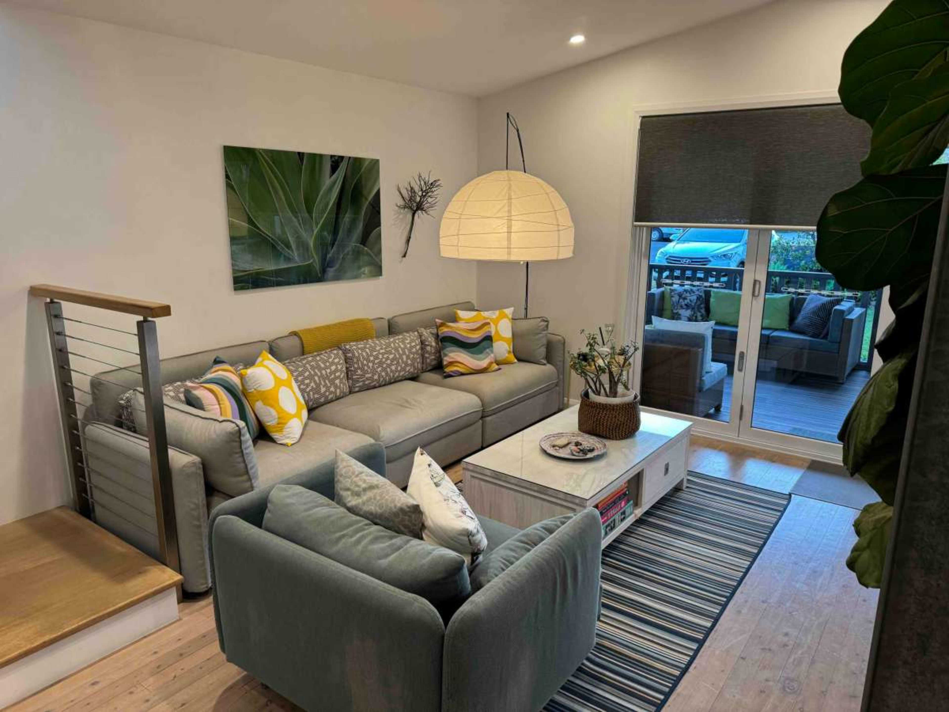 The image shows a modern living room featuring a sectional couch, a coffee table, and large windows that open to a balcony.