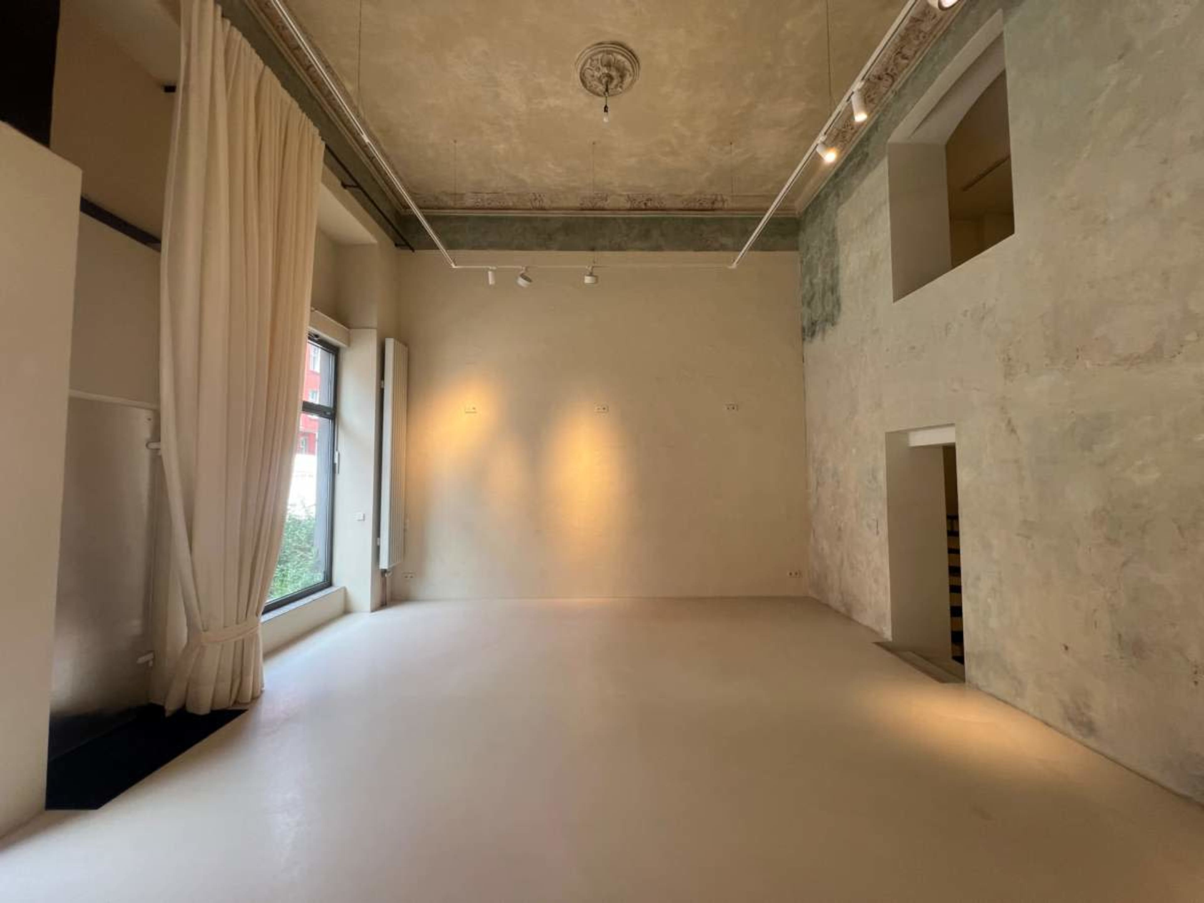 The image shows a spacious, minimalist interior with light-colored walls, large windows, and a polished floor.