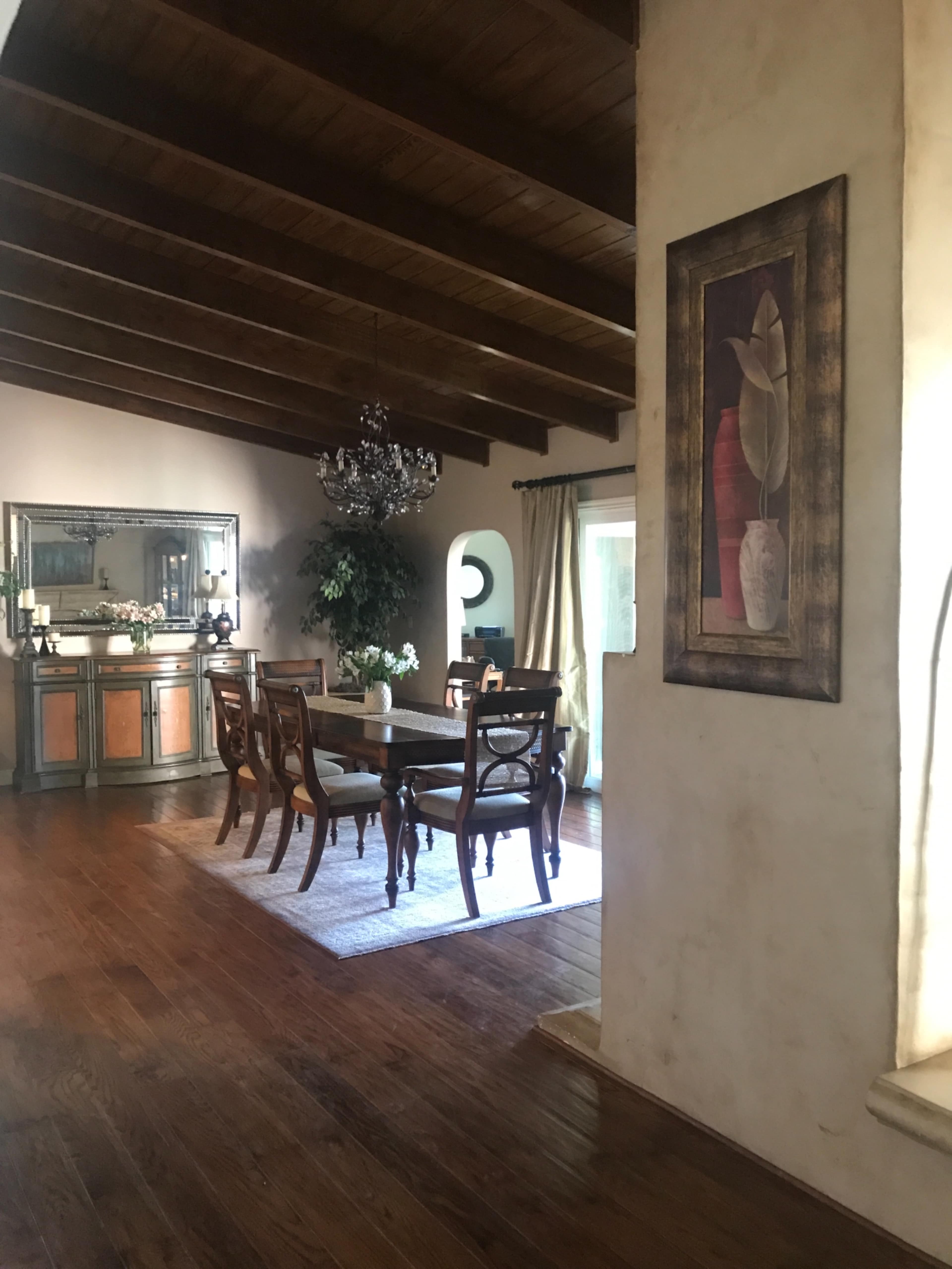 A dining area with a wooden table, chairs, and a chandelier under a ceiling with exposed beams.
