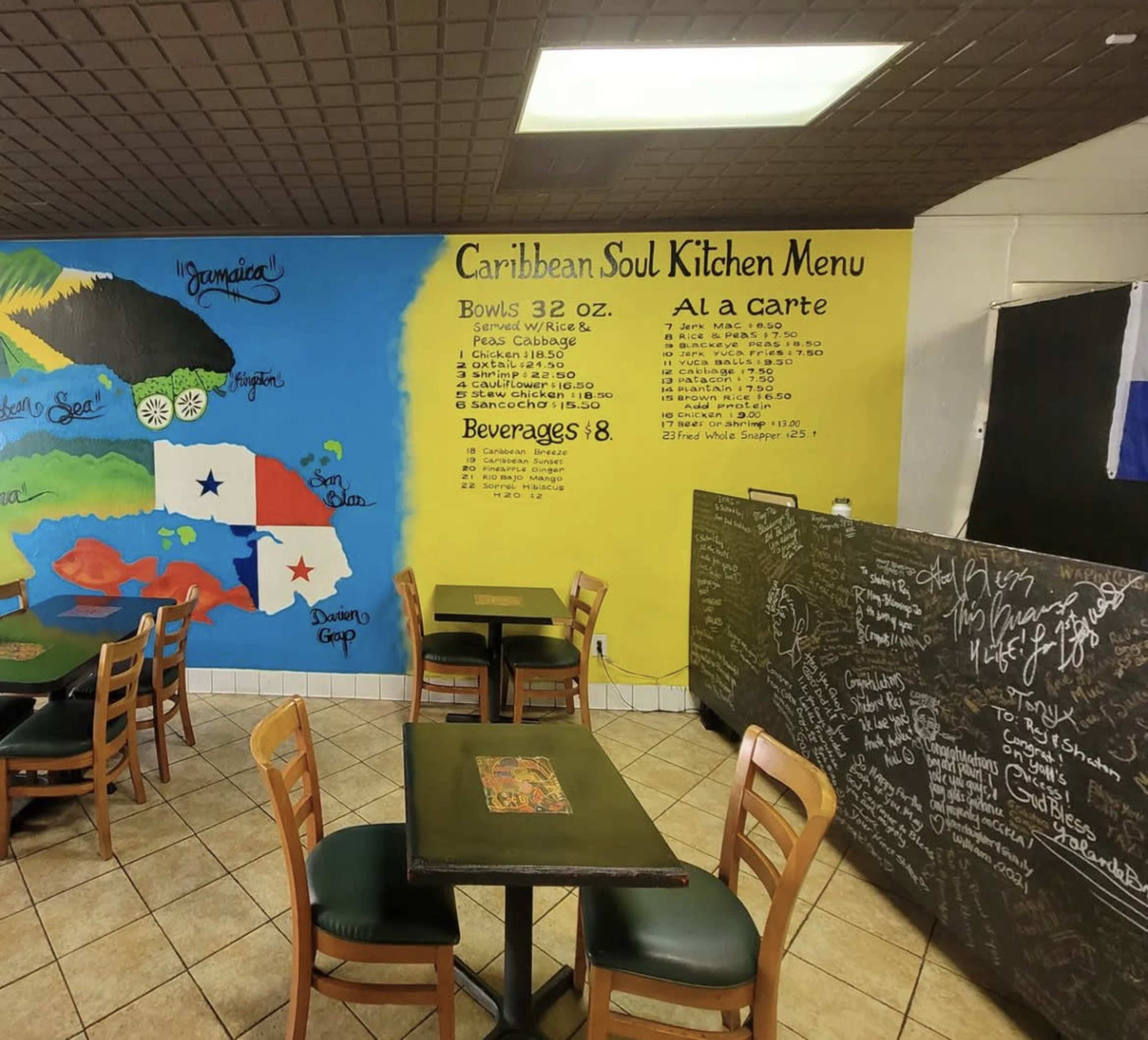 A Caribbean-themed restaurant interior with a colorful mural depicting the Caribbean islands on the wall and a menu list hand-painted in yellow.