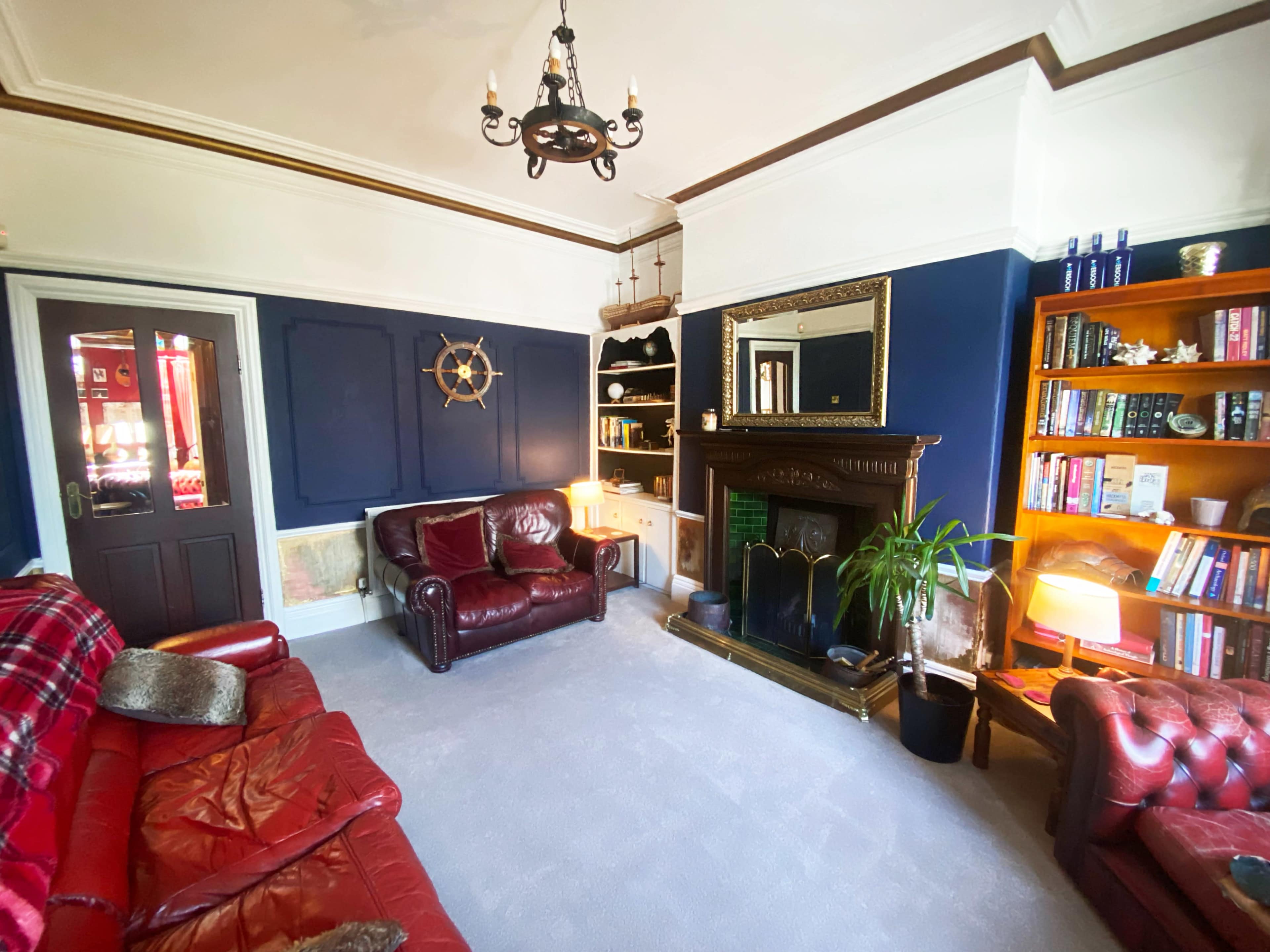 The living room features two red leather sofas, a dark blue accent wall, a bookshelf filled with books, and a decorative fireplace.