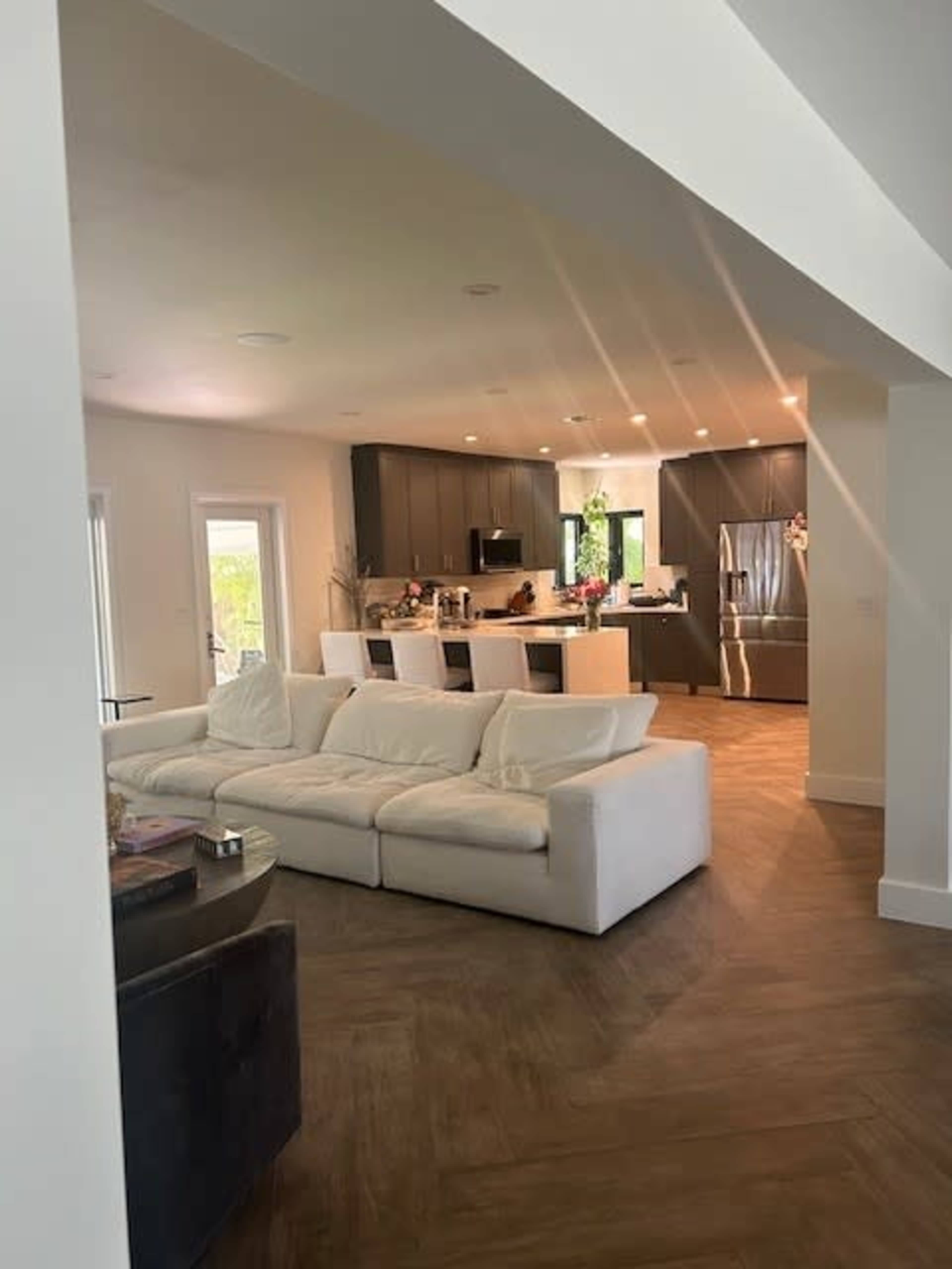 A spacious open-concept living area features a white sofa and a modern kitchen with dark cabinetry in the background.