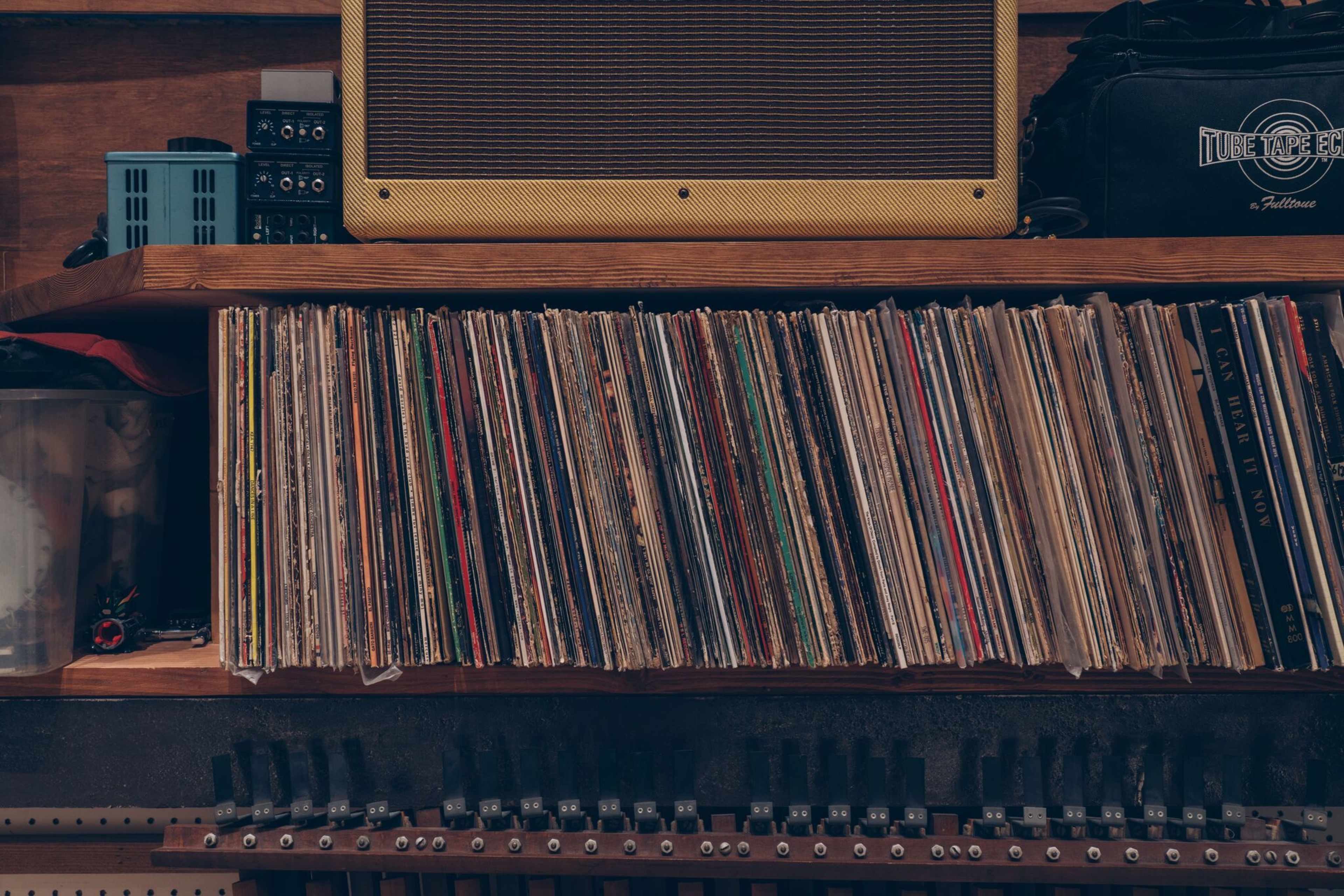 A wooden shelf displays a collection of vinyl records alongside an amplifier and various audio equipment.