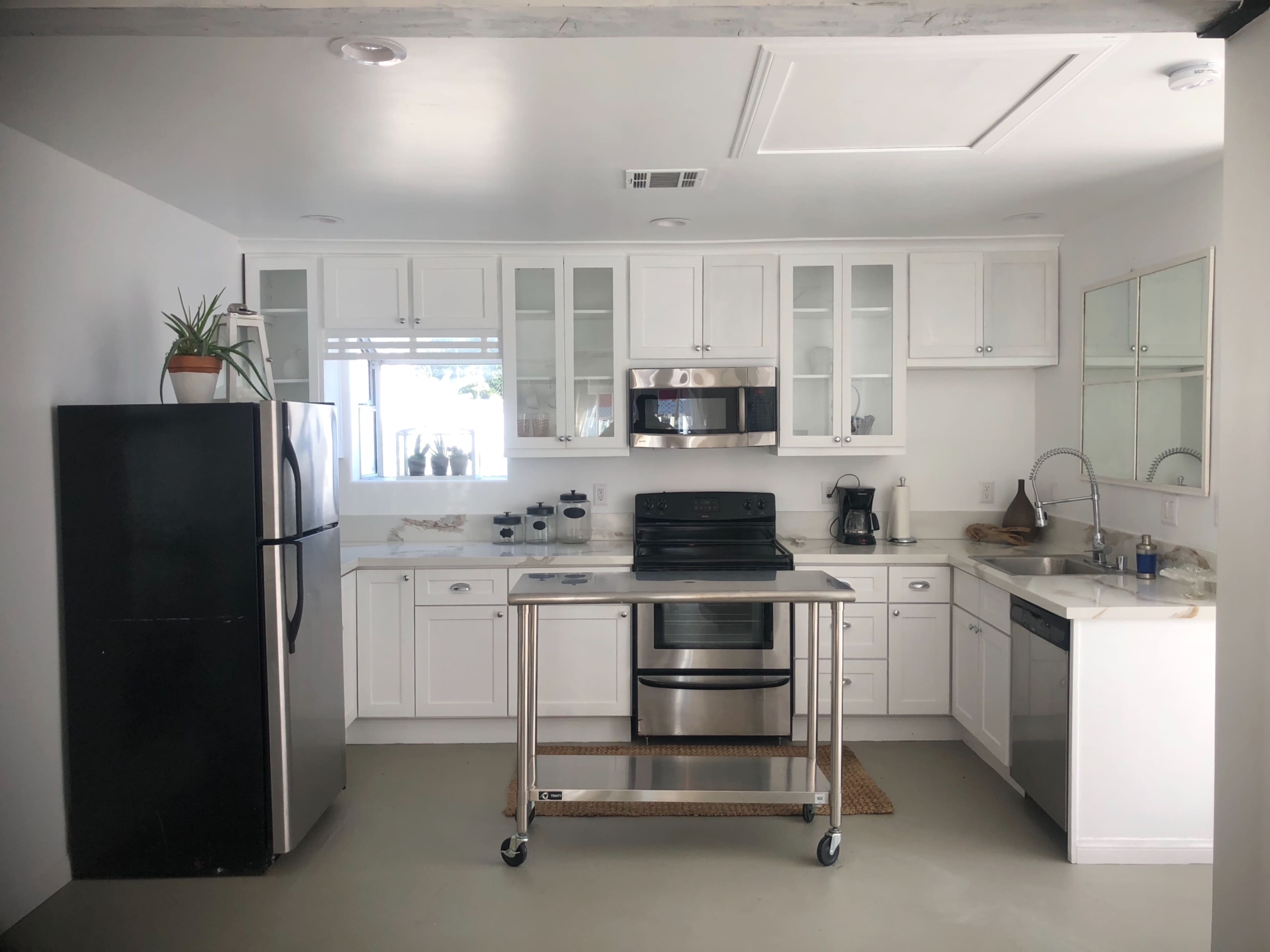A modern kitchen with white cabinets, stainless steel appliances, and a central cart on wheels.