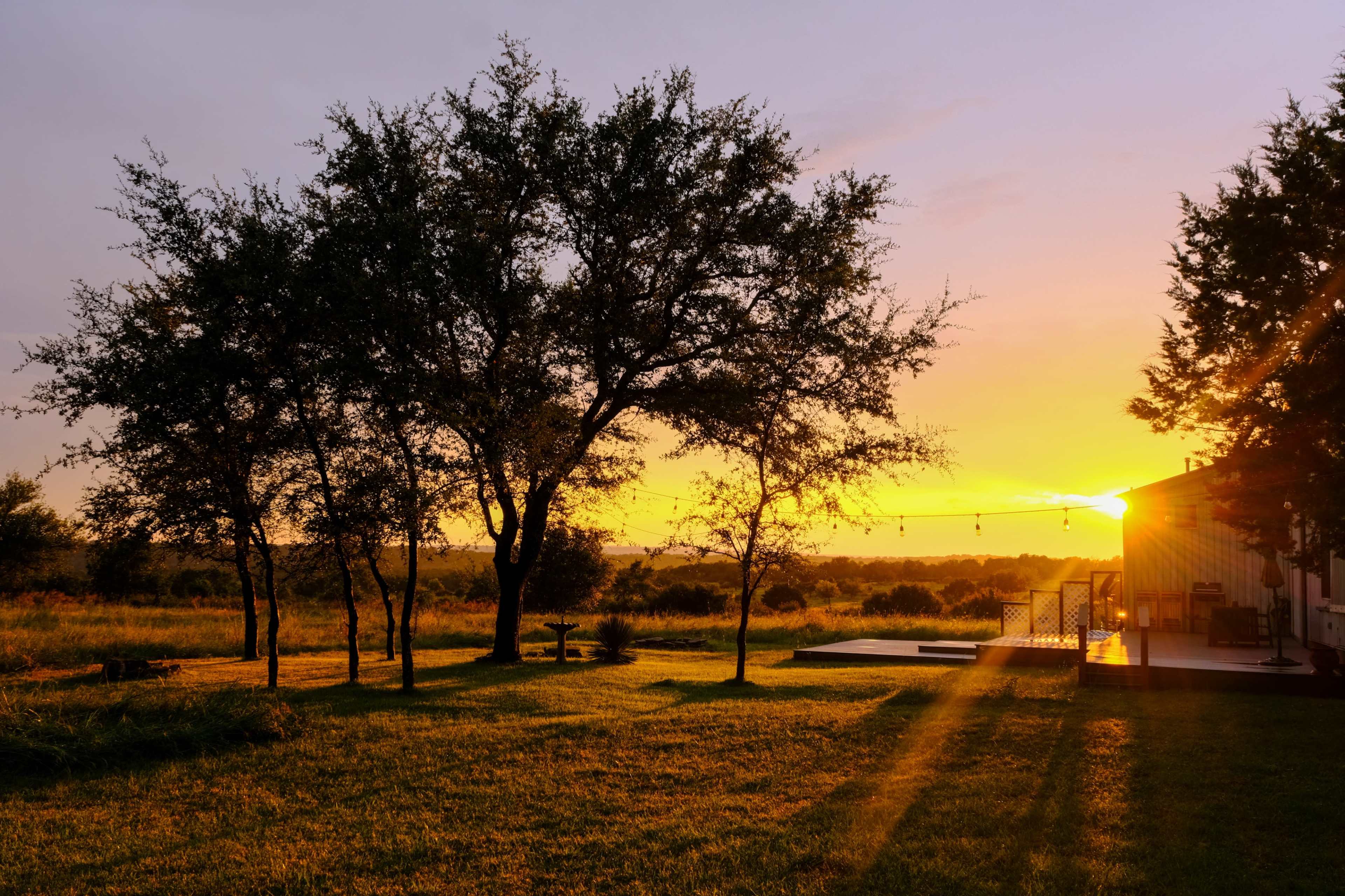 A sunset over a grassy field with silhouetted trees and a modern deck area.