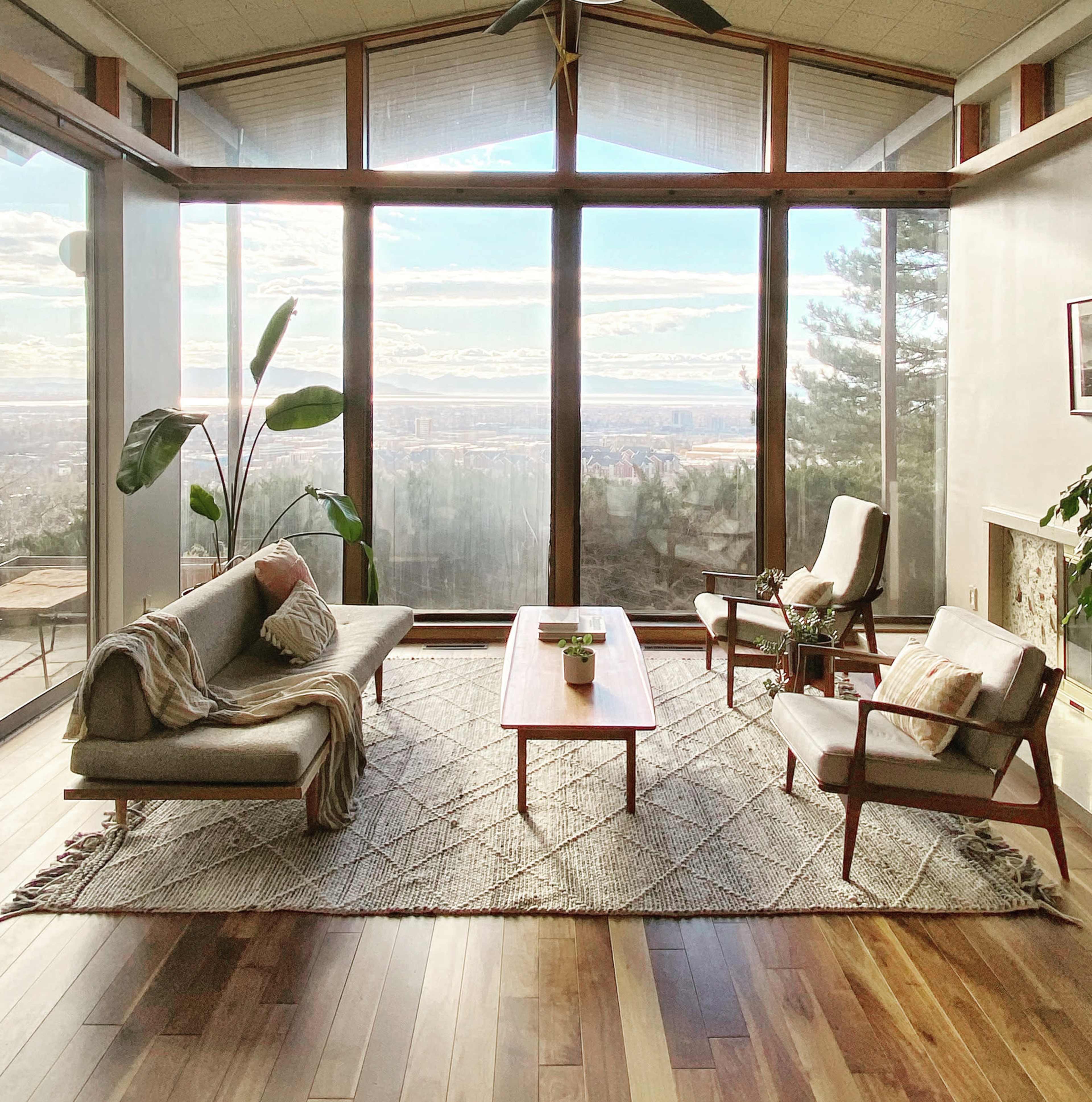The living room features a large window with a view of the landscape, furnished with a sofa, two armchairs, a coffee table, and a plant.