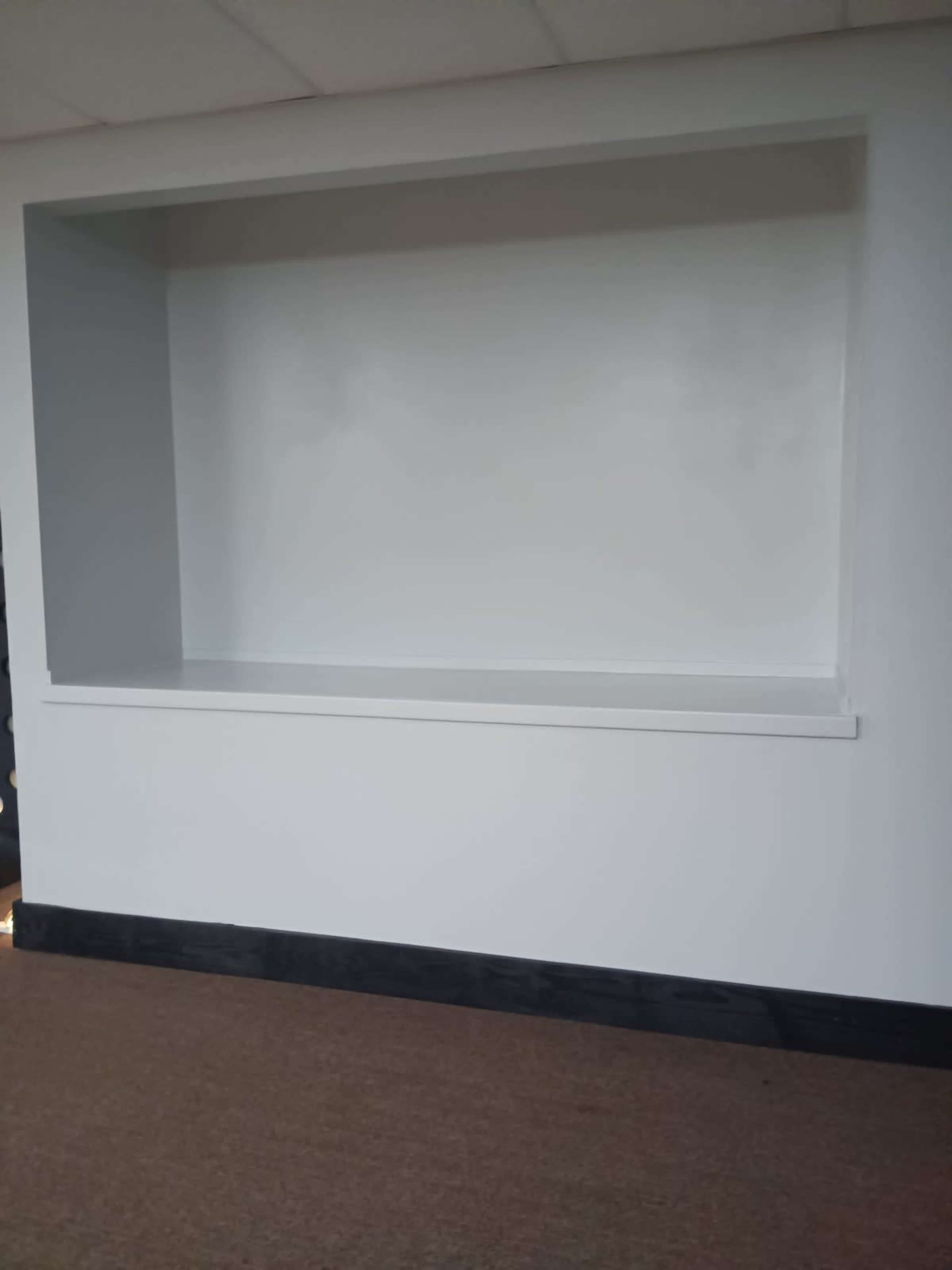 The image shows a large, empty, white recess in a wall with a smooth surface and a shelf below it.