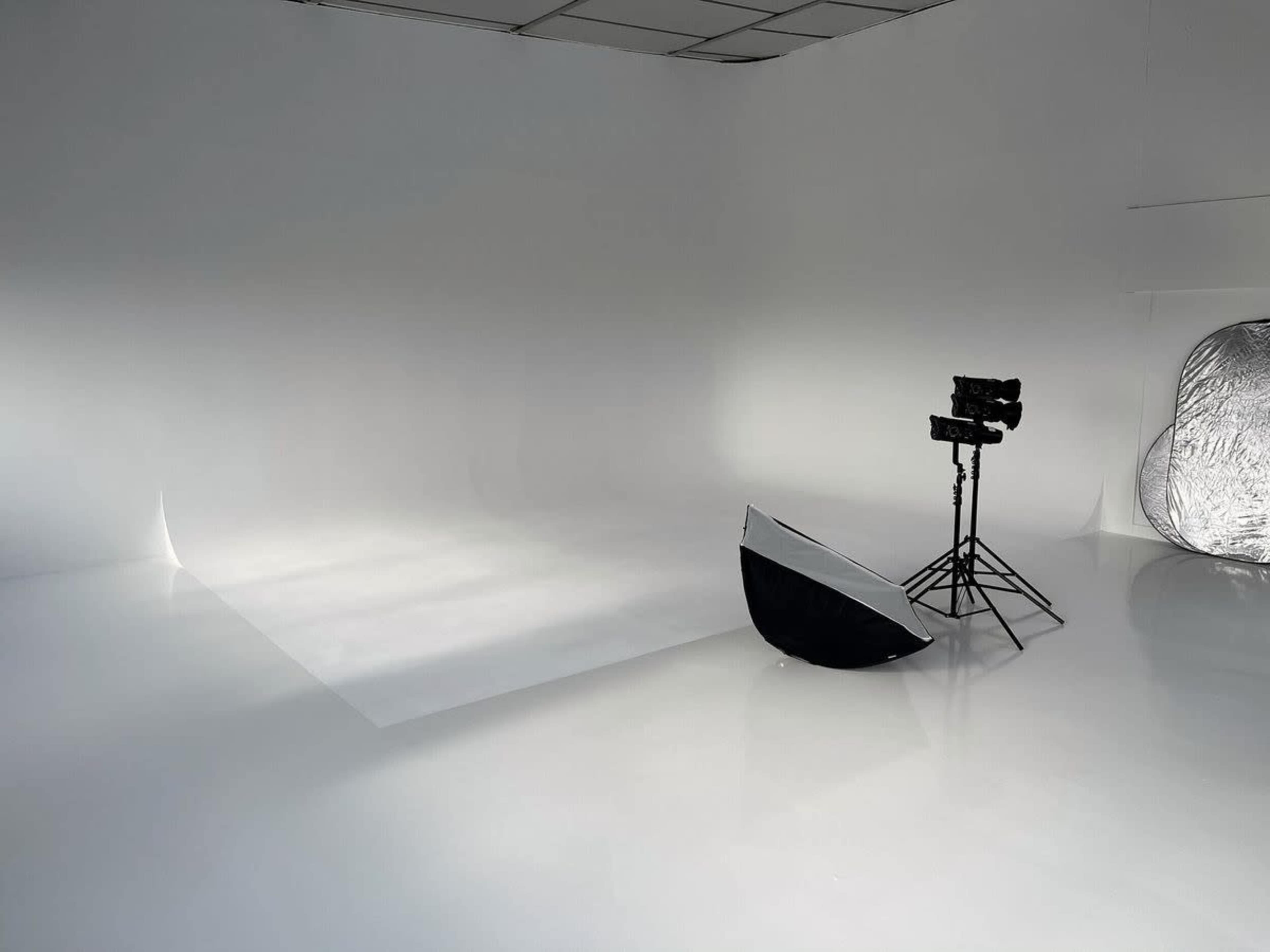 A bright photography studio features a large, reflective white floor, a backdrop, and lighting equipment positioned on a stand.
