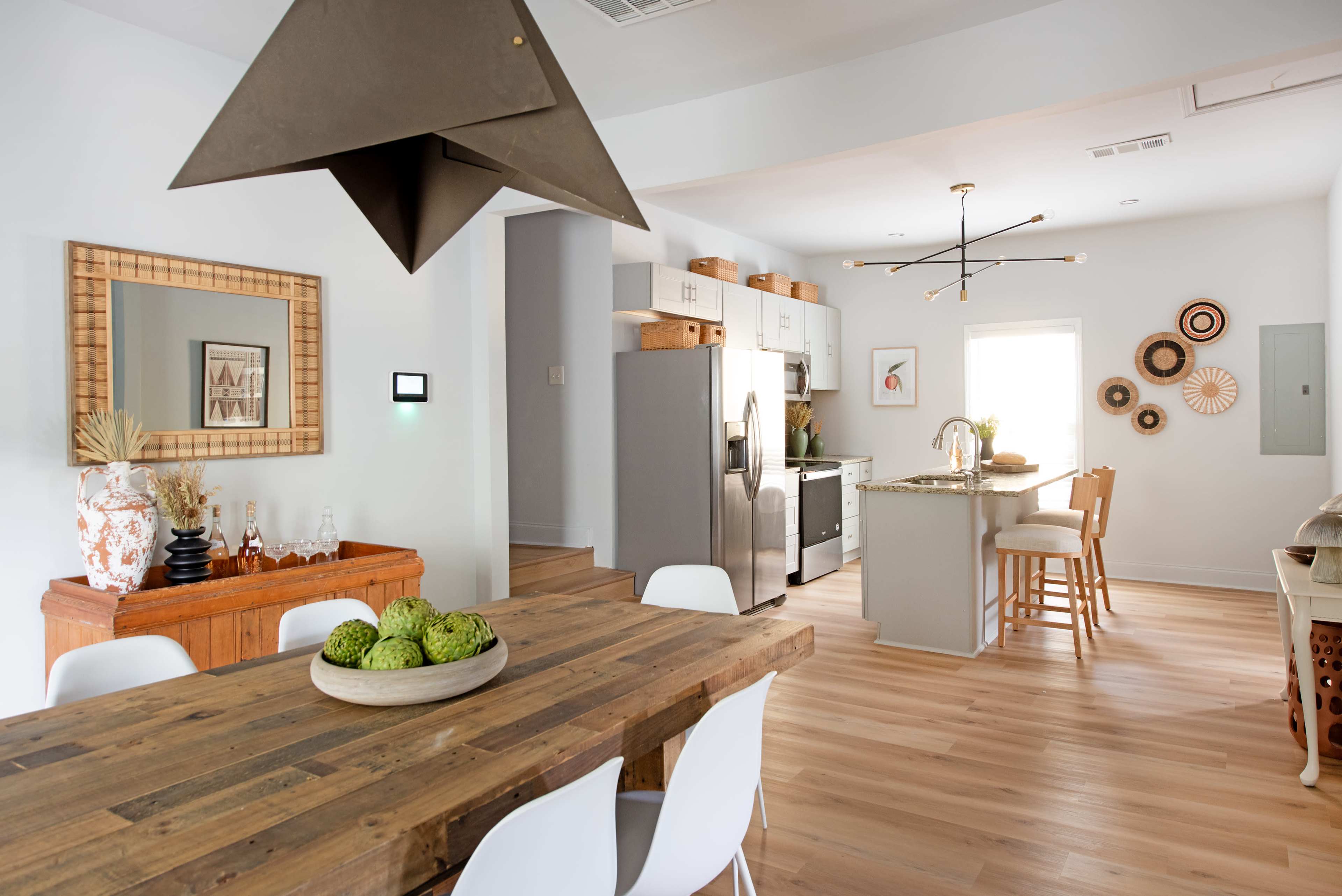 The image shows a modern kitchen and dining area with a wooden dining table, metal pendant light, and a mix of cabinetry and appliances.