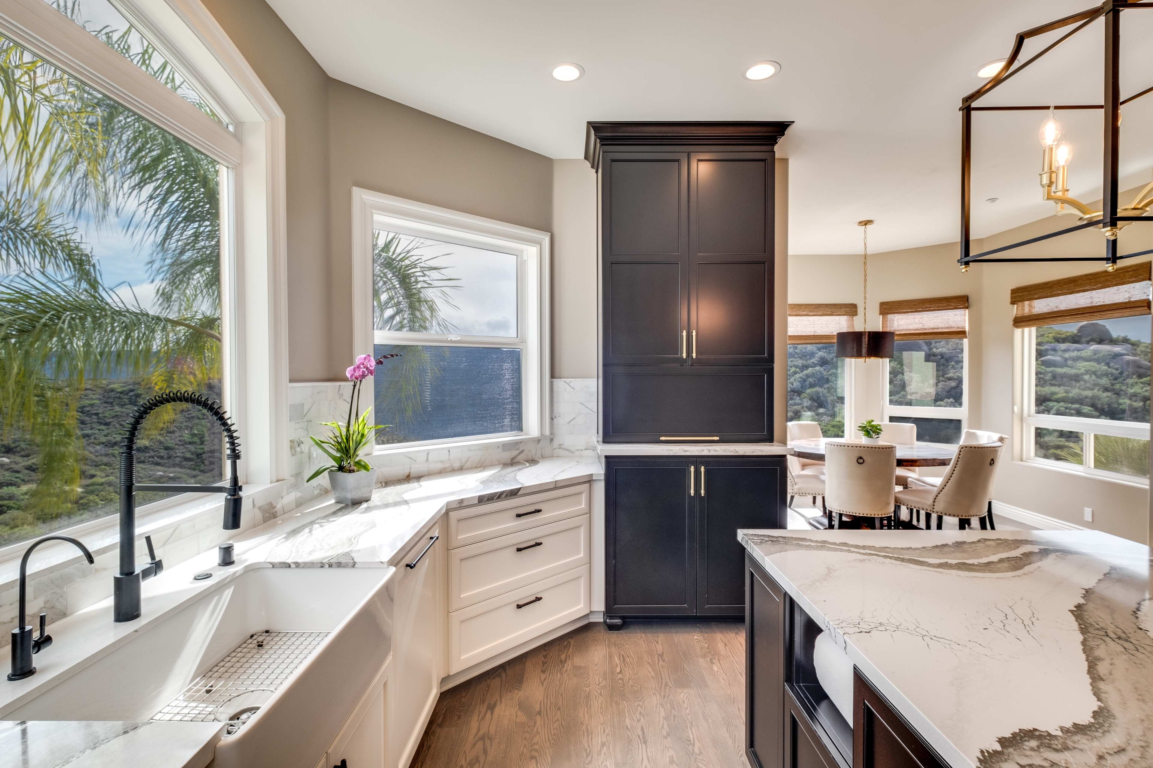The image shows a modern kitchen featuring dark cabinetry, a white marble countertop, and a large window with a view of greenery.