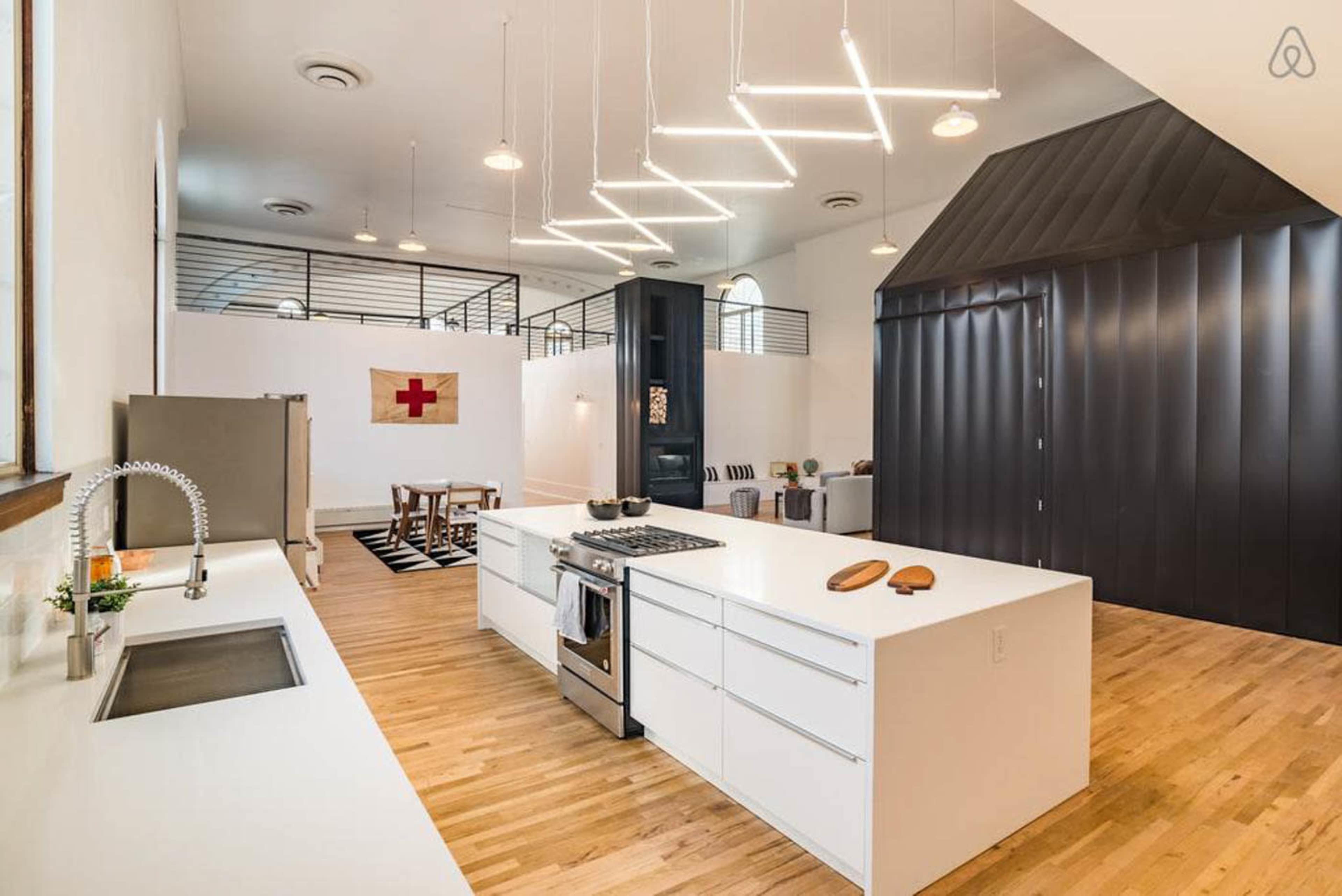 A modern kitchen with a large white island, stainless steel appliances, and an open dining area featuring a wooden table and minimalist decor.