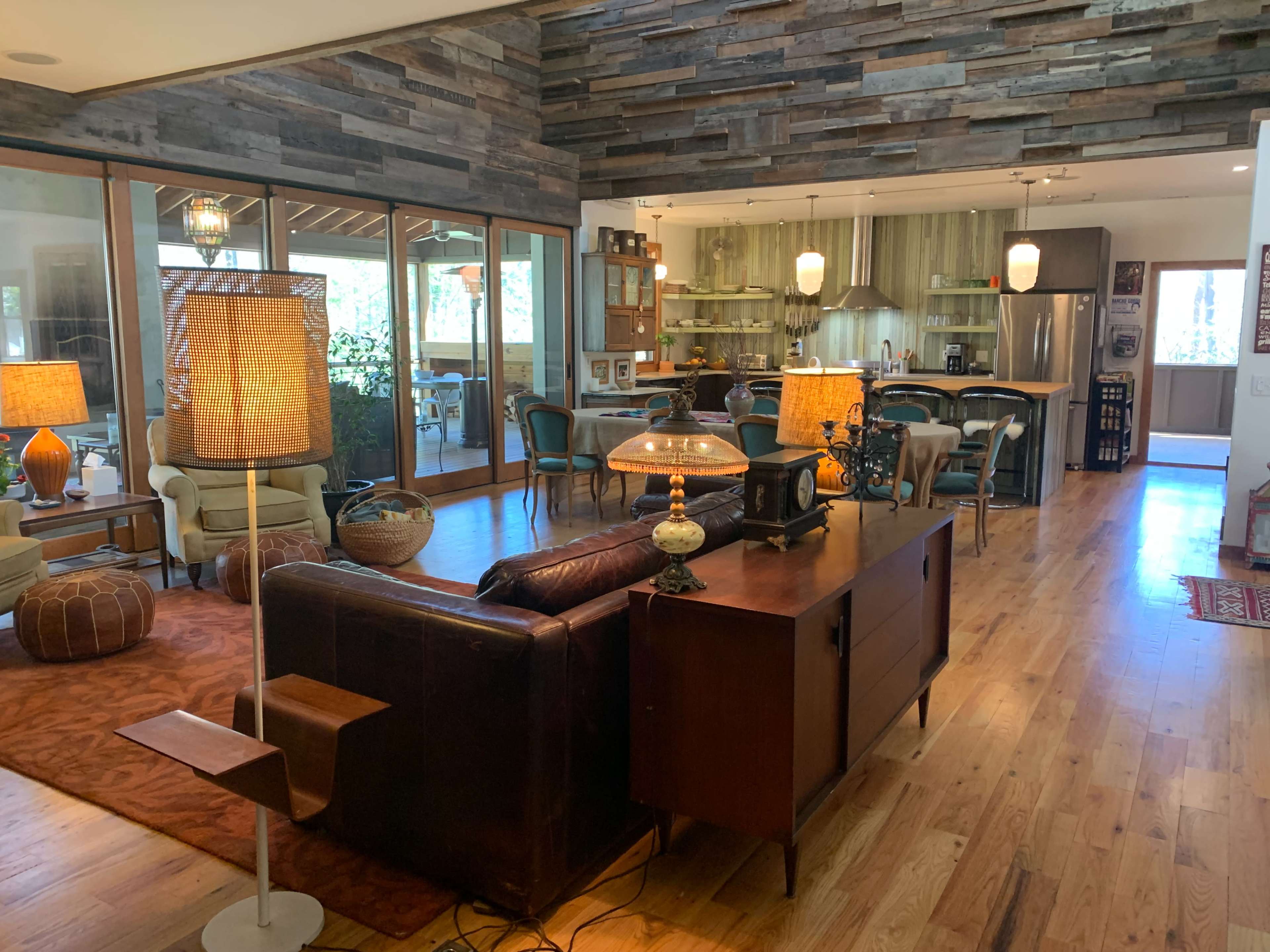 A spacious living area with a view of a modern kitchen, featuring mid-century furniture, wooden accents, and large windows that allow natural light to enter.