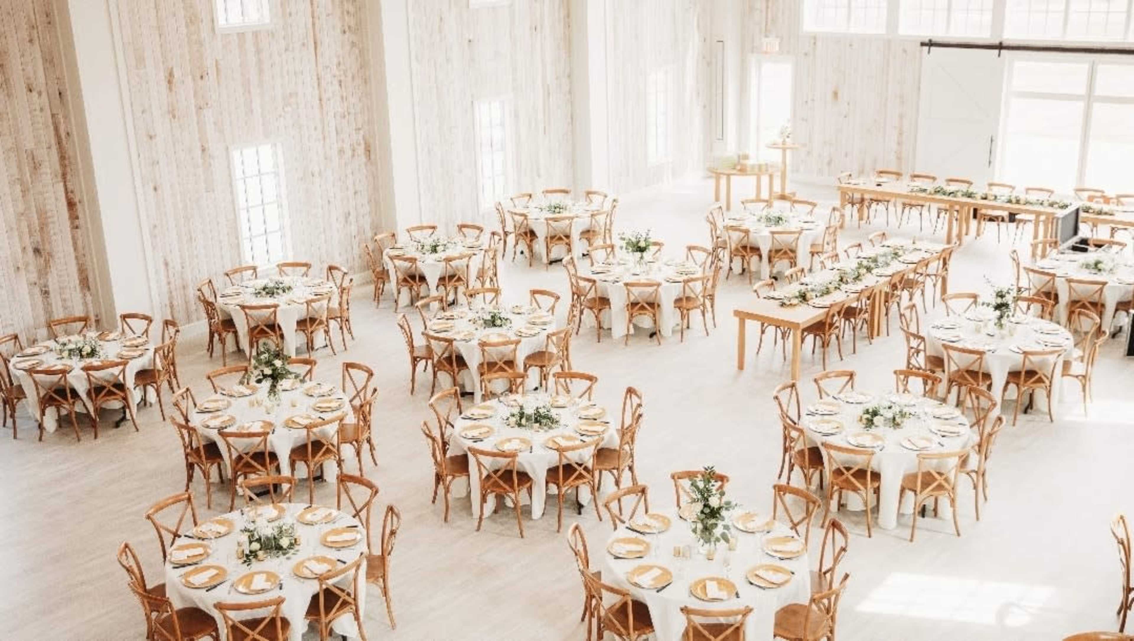 The image shows a decorated event space with round tables set for dining, arranged neatly in a bright, wooden-paneled room.
