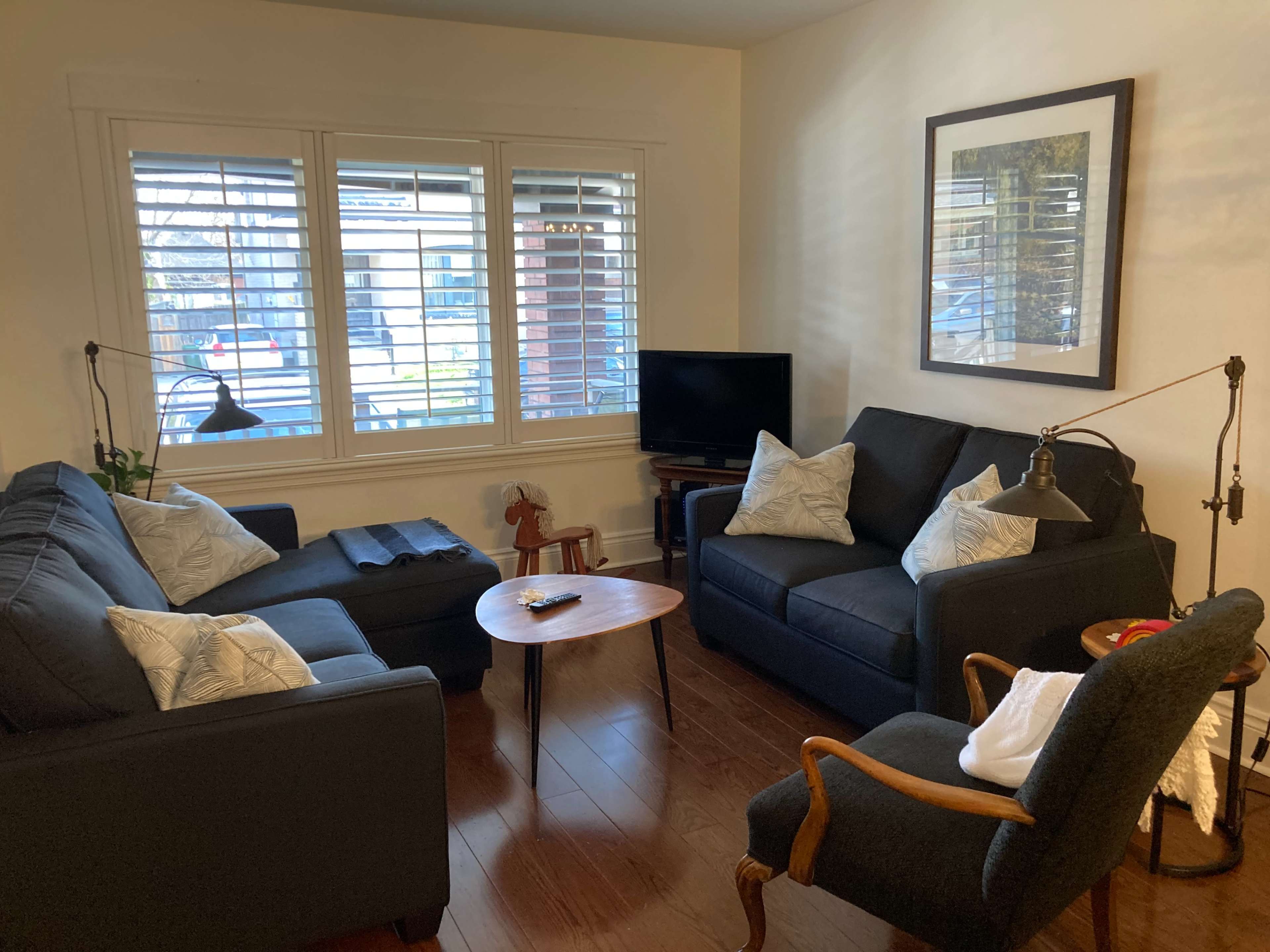 A small living room with two dark sofas, a wooden coffee table, a television, and a window with shutters.