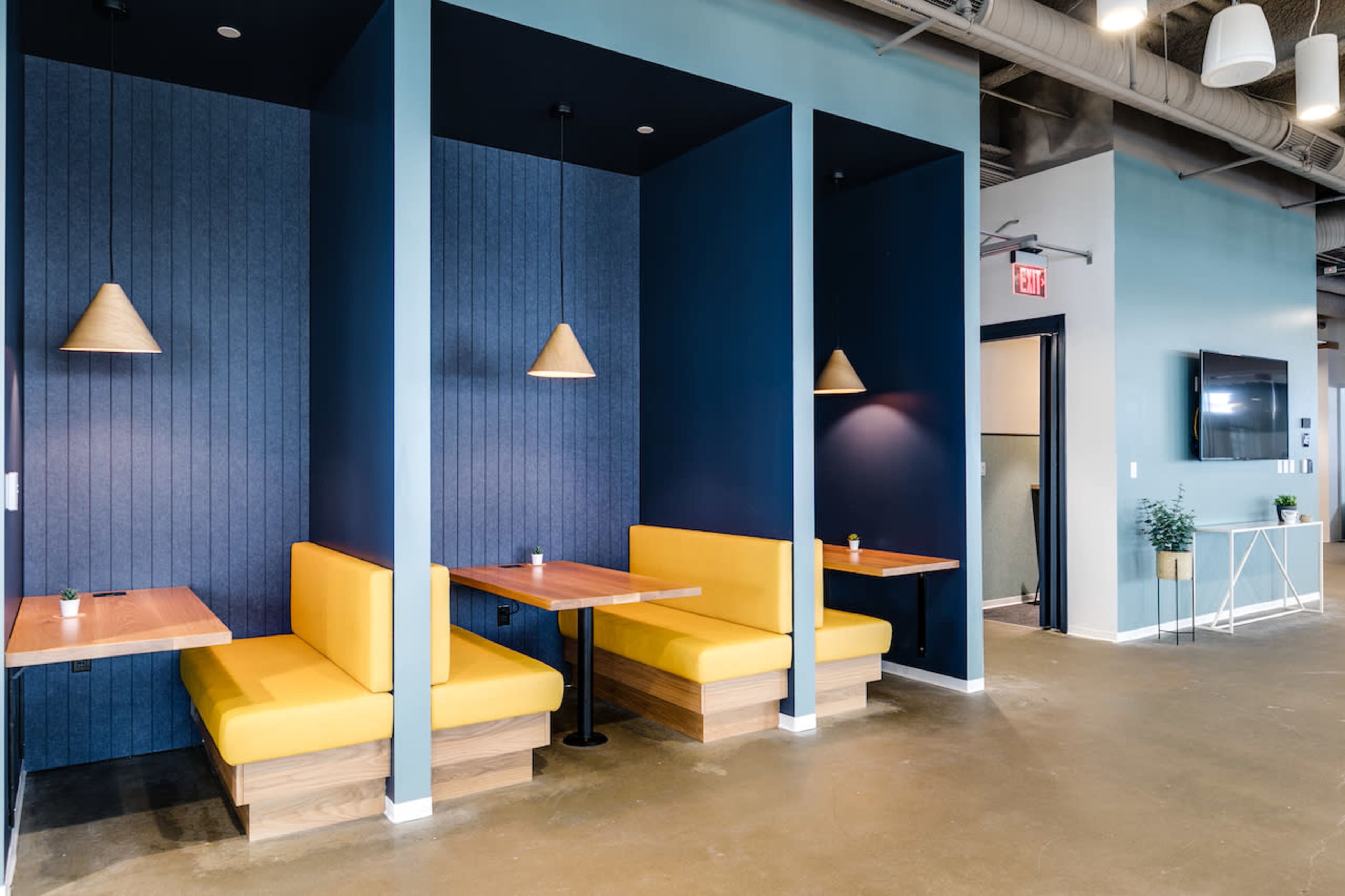 A modern, minimalist café with yellow booths against a blue wall, illuminated by pendant lights.