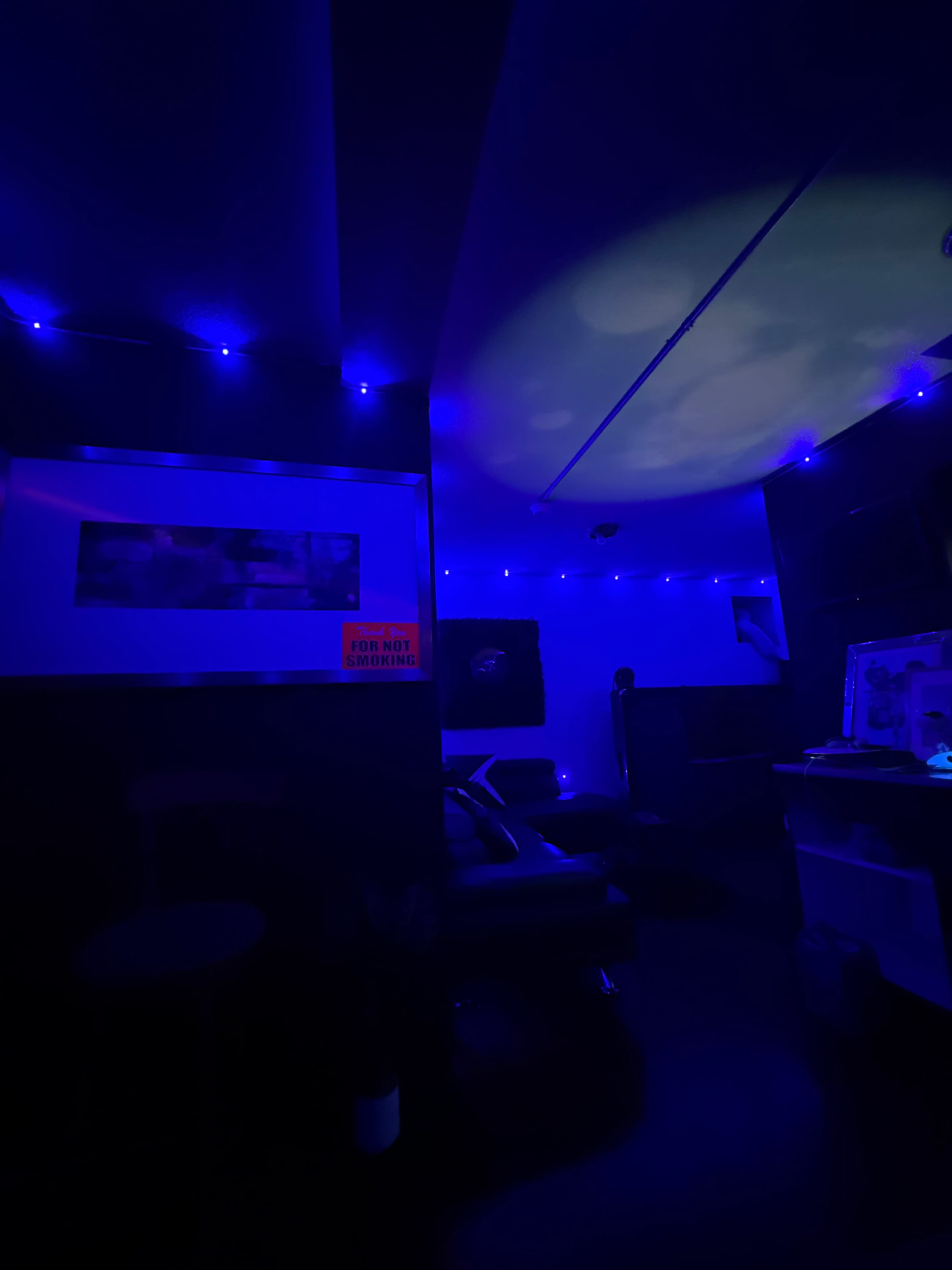The image shows a dimly lit room with blue ambient lighting, featuring a modern sofa, wall decor, and a sign that reads "FOR NOT SHARING."