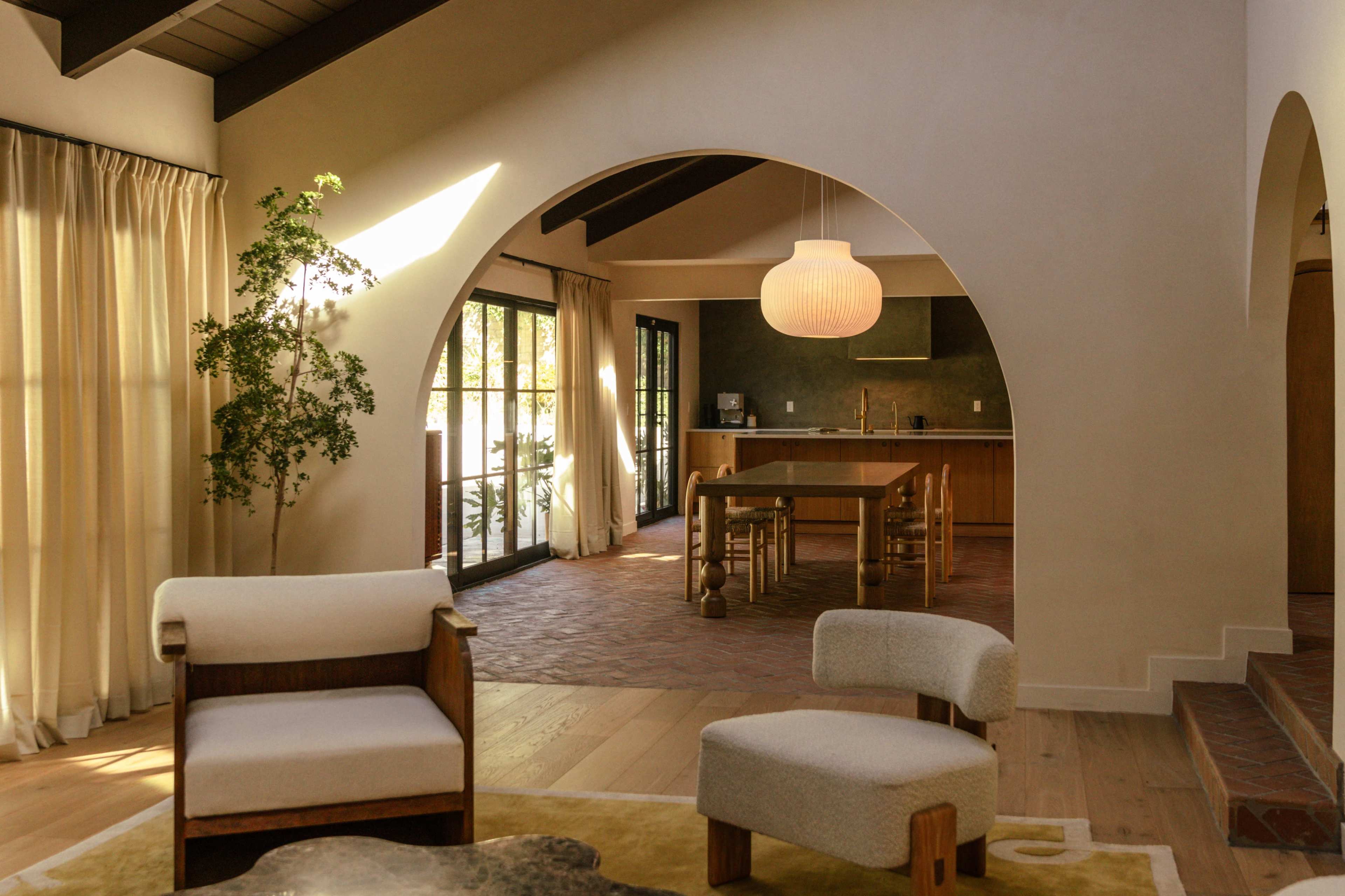 A spacious indoor area features two upholstered chairs, a wooden dining table, and large windows with soft drapes letting in natural light.