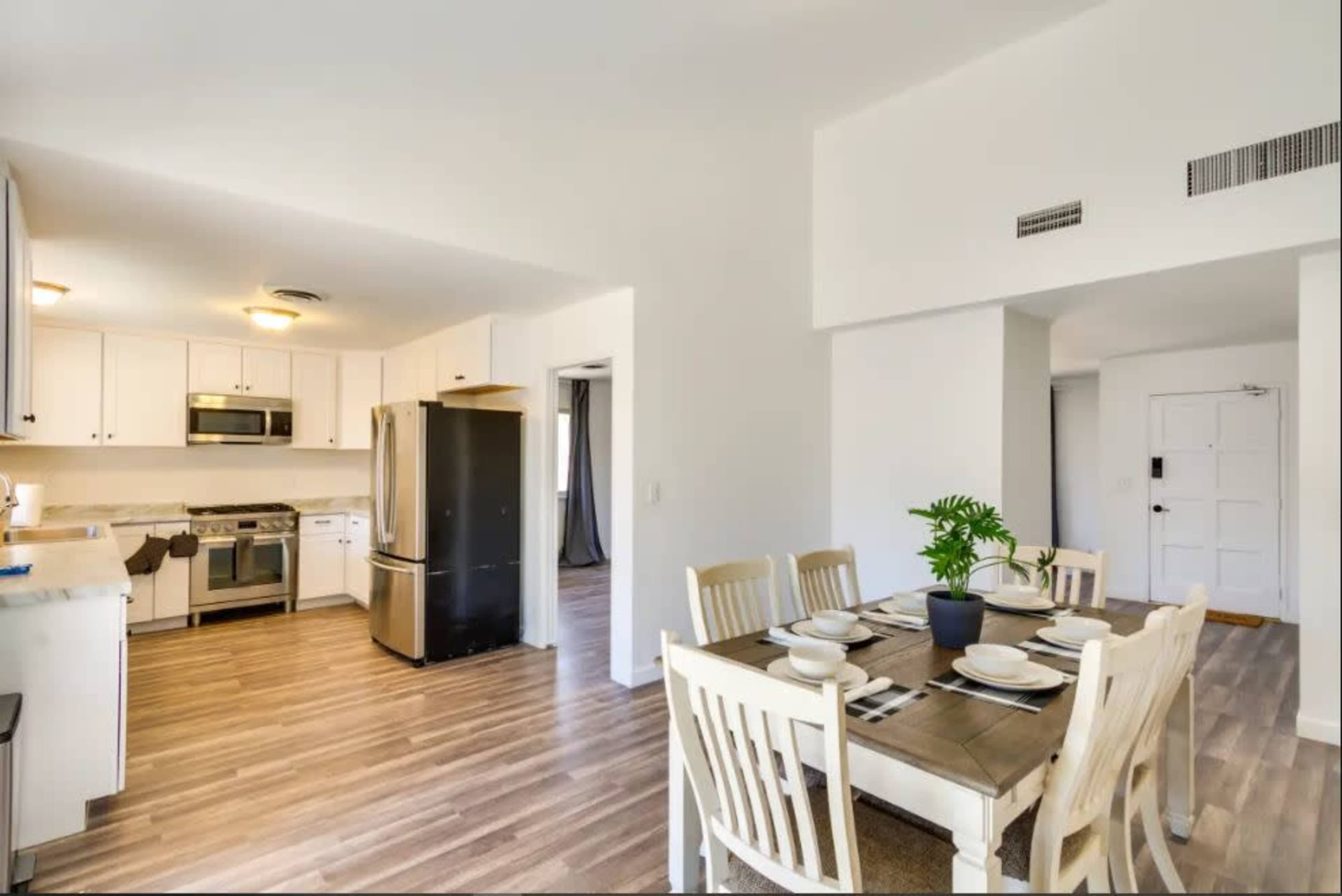 A modern kitchen and dining area featuring stainless steel appliances, a dining table set for six, and light-colored cabinetry.