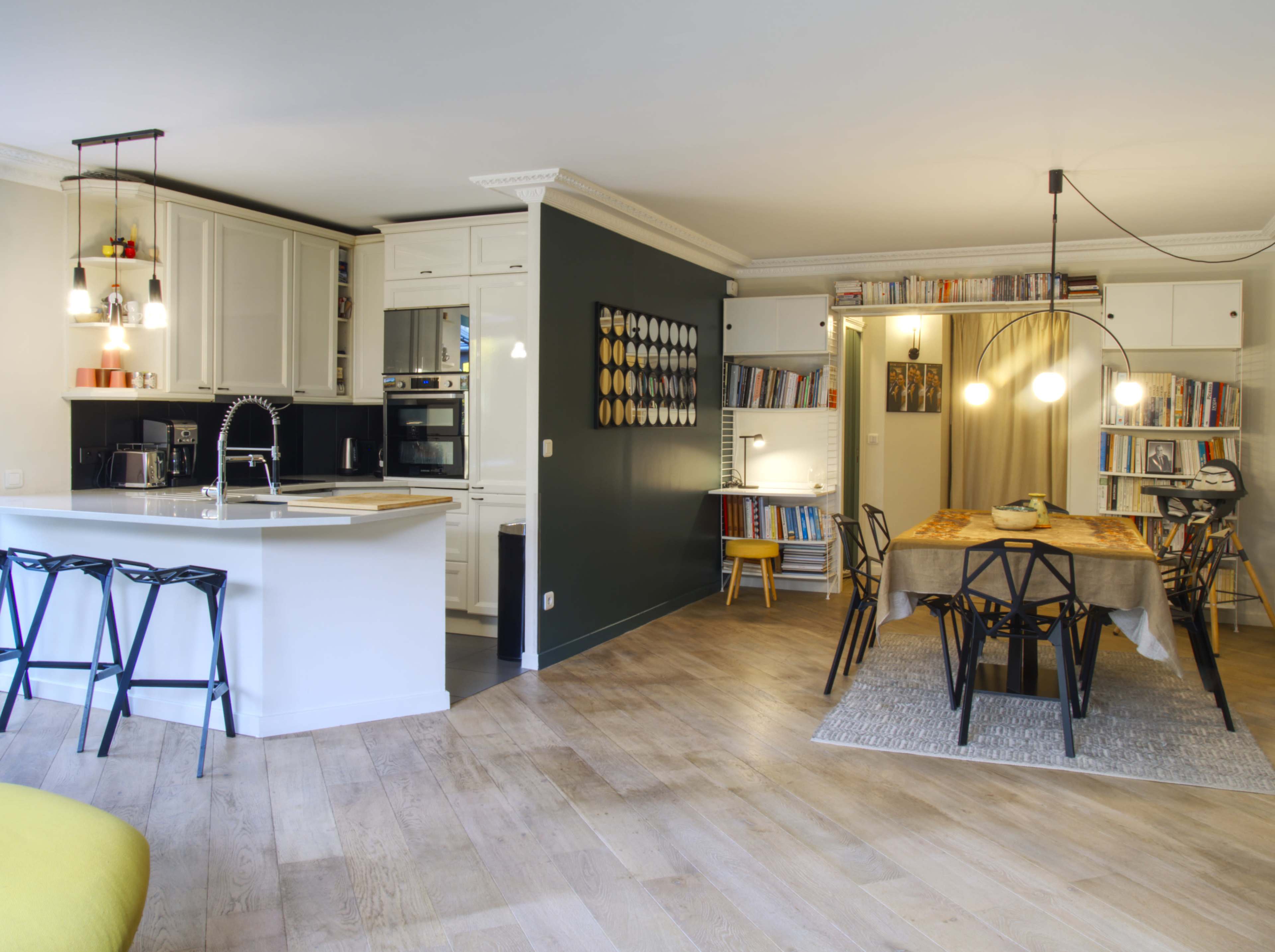 The image shows a modern open-concept kitchen and dining area with wooden flooring, white cabinetry, and a dining table surrounded by black chairs.