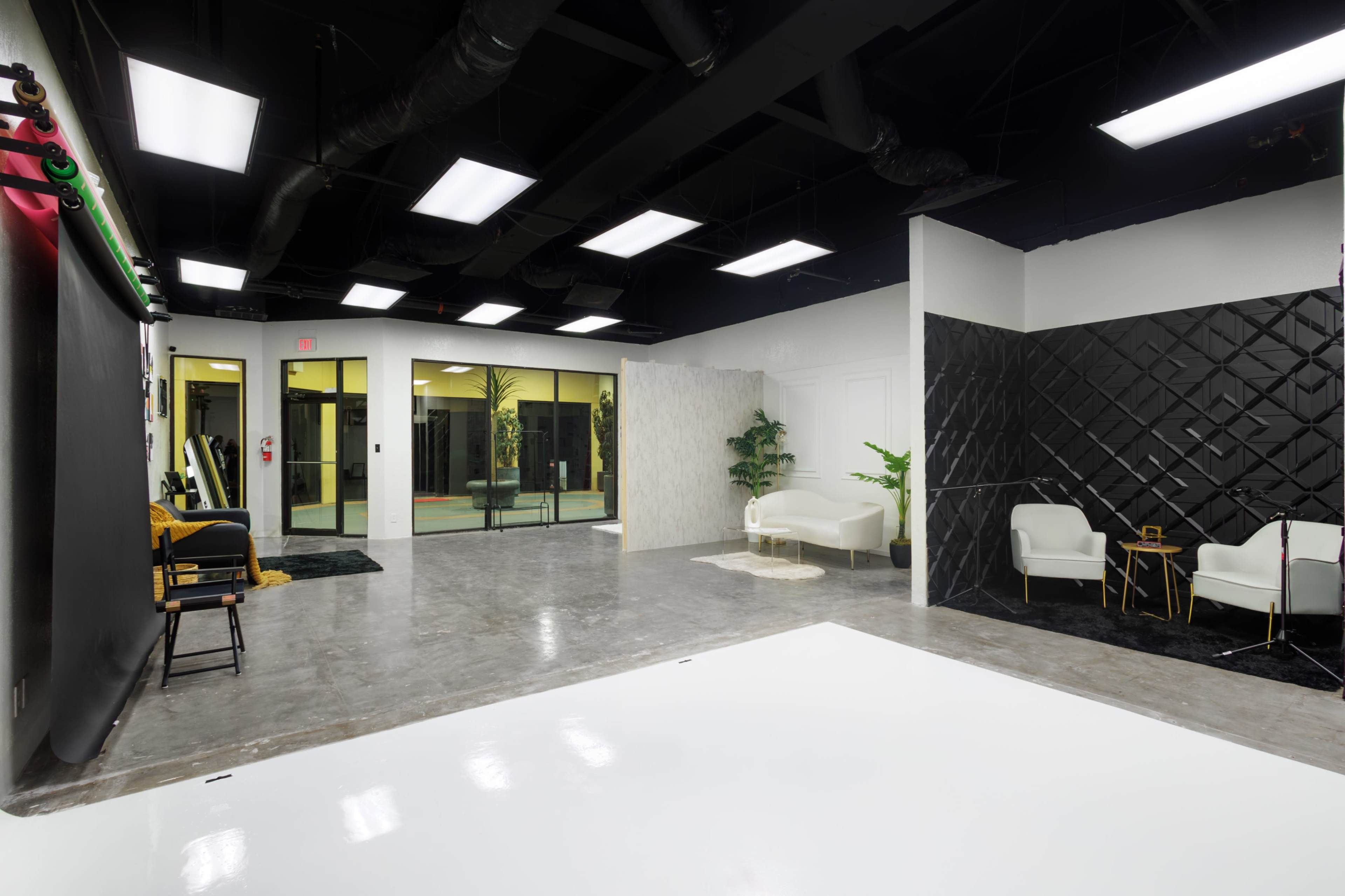 A modern, open studio space with black and white walls, large windows, and minimalist furniture arranged in different areas.