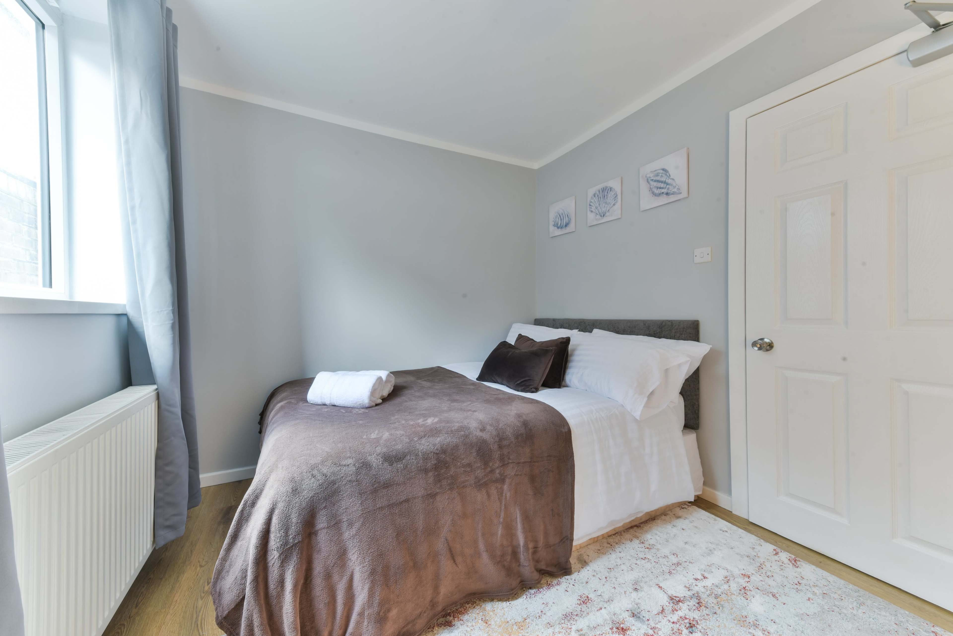 A neatly made bedroom with a single bed, a radiator, and framed pictures on the wall.