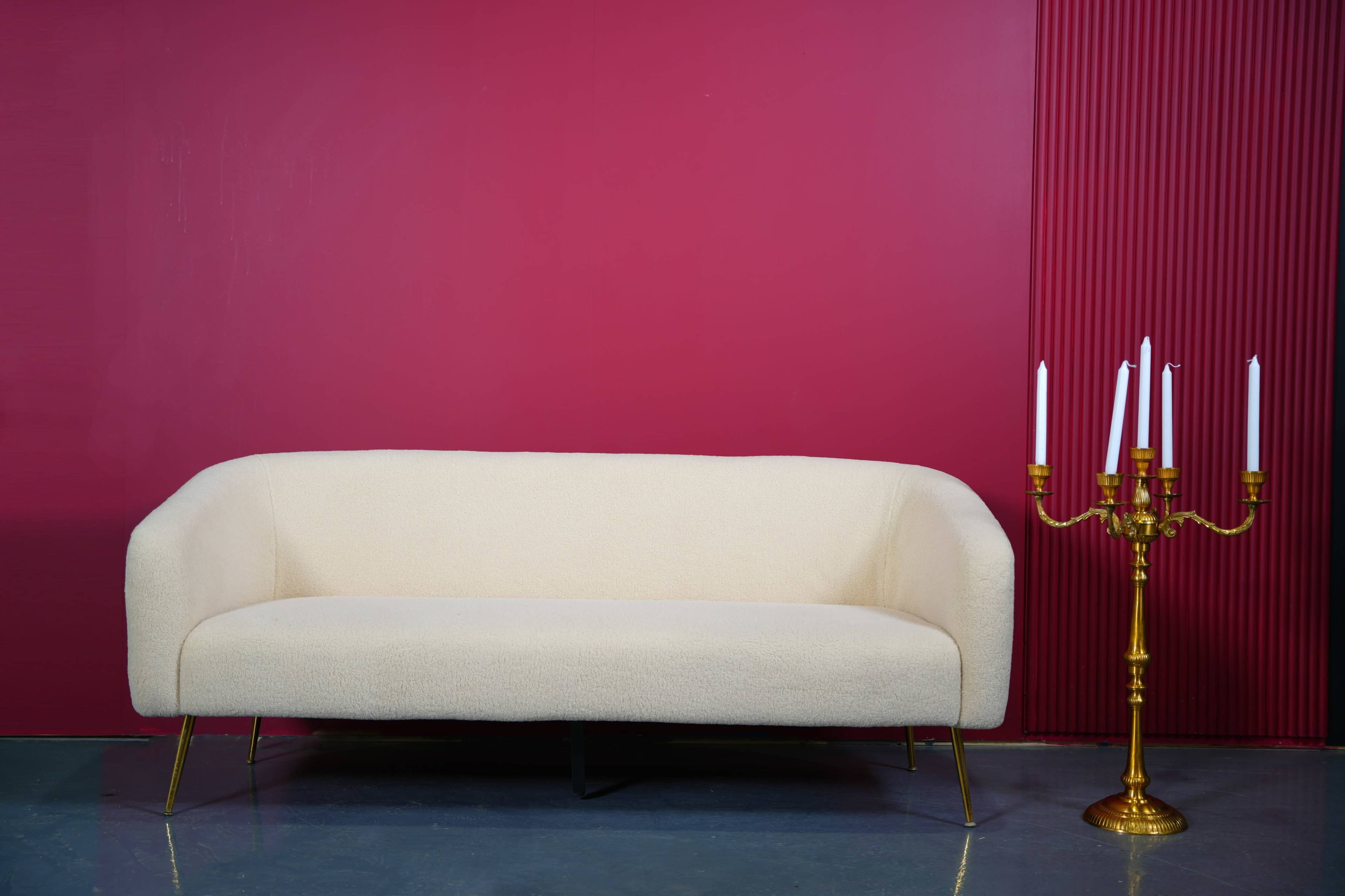 A cream-colored couch is placed against a deep red wall, alongside a gold candelabra with five white candles.