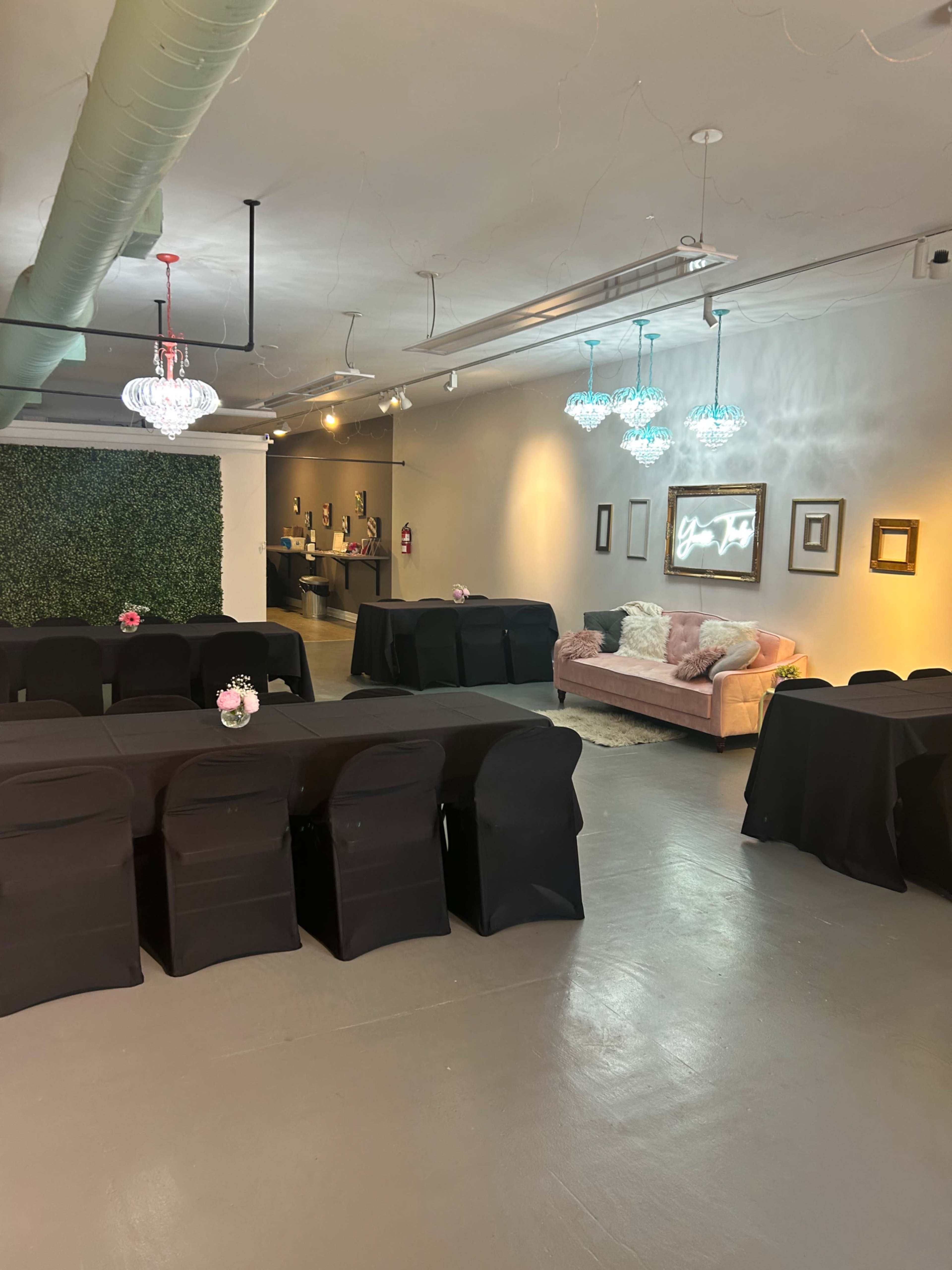 An event space with black-covered tables arranged in rows, a light pink couch, and decorative lighting on the walls.