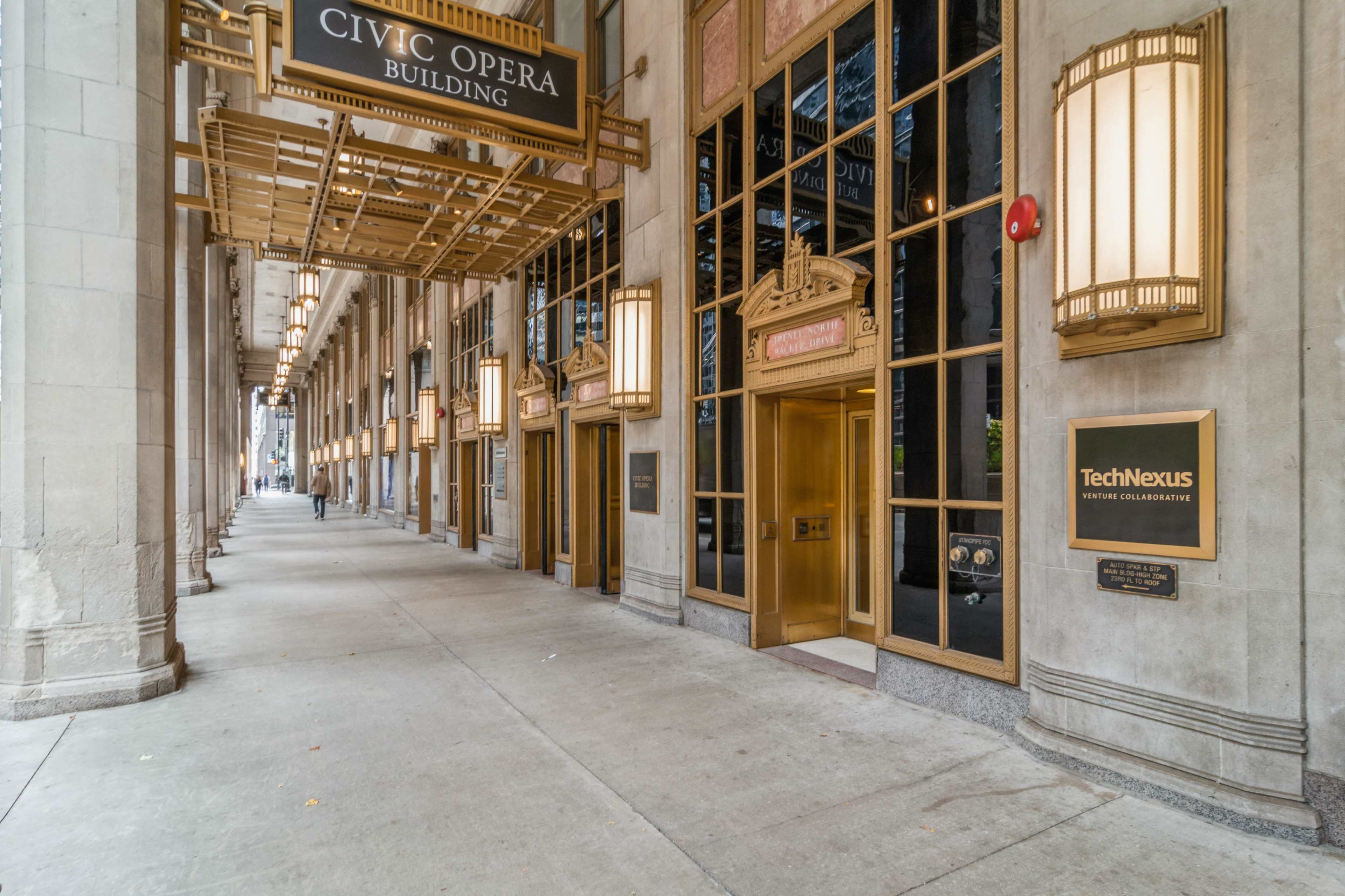 The image shows the entrance of the Civic Opera Building, featuring large glass doors and decorative lighting along the walkway.